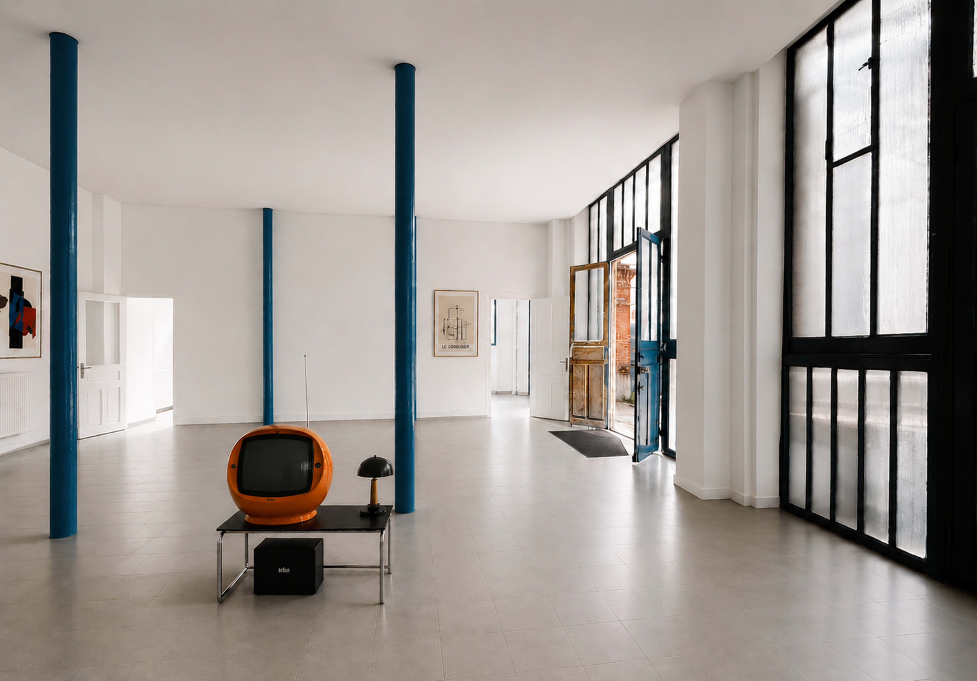 The image shows a modern interior space featuring a retro orange television on a metal table, with large windows allowing natural light to fill the room.