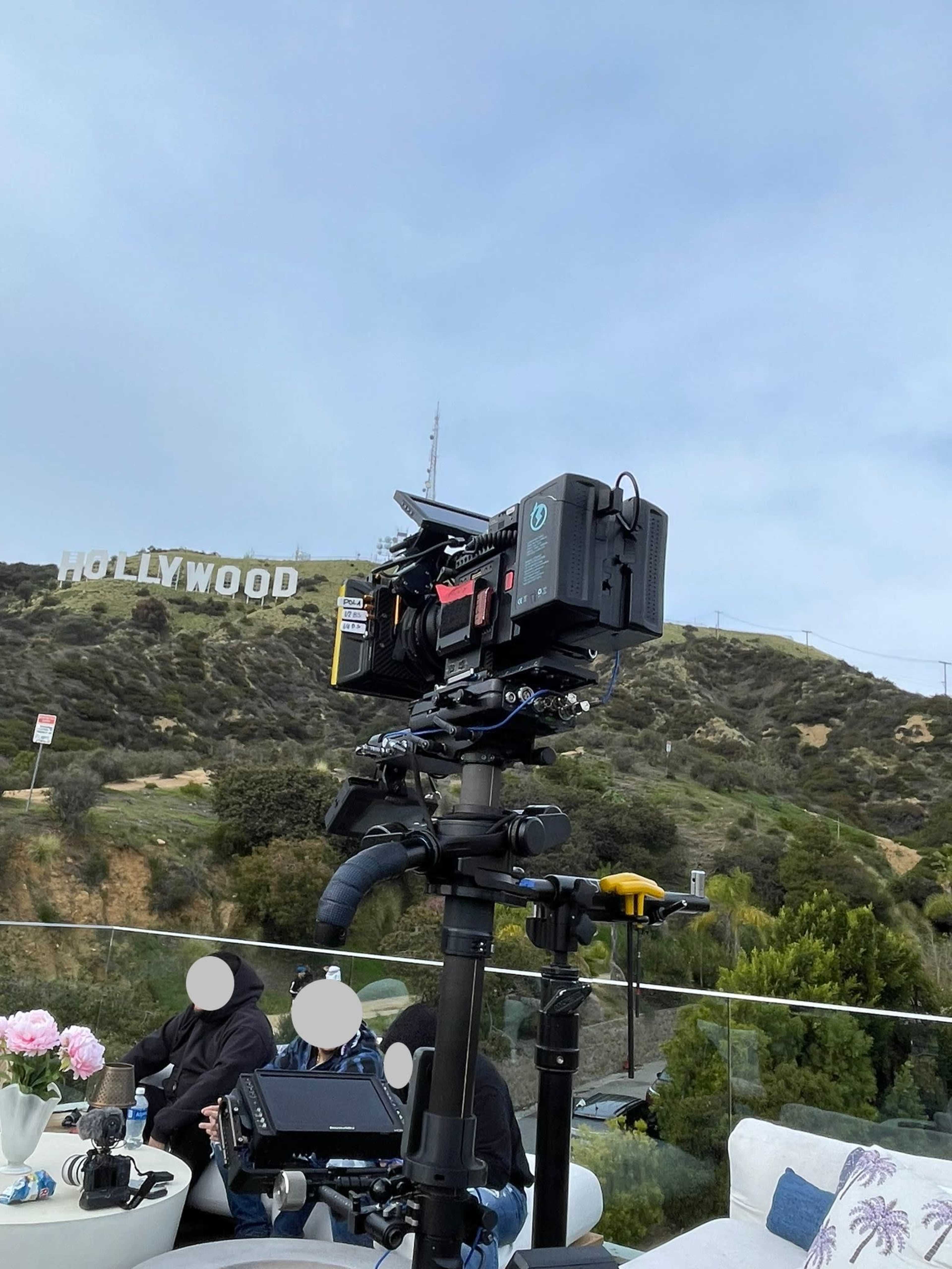 A camera is set up on a tripod with the Hollywood sign visible in the background.