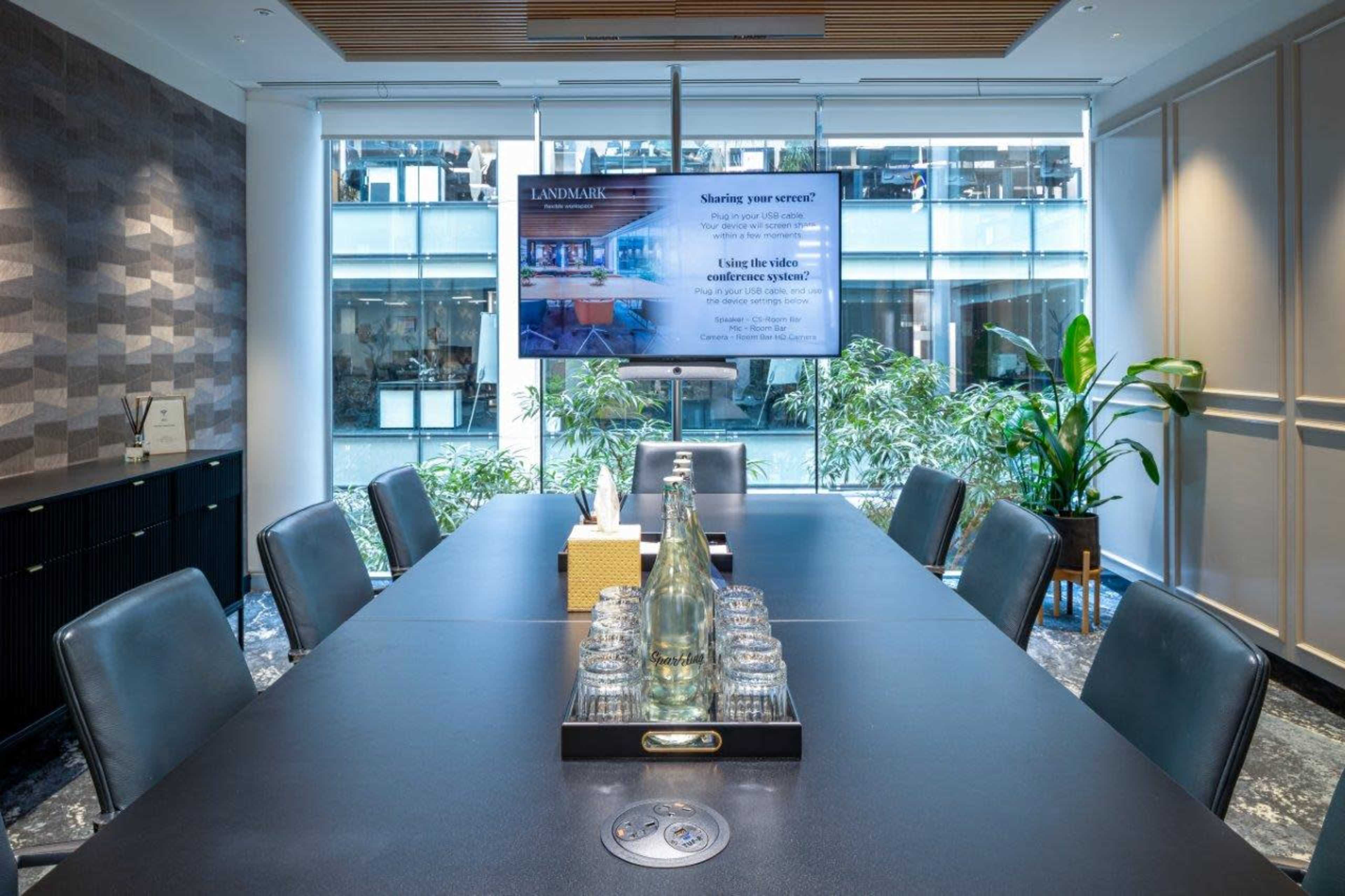 A modern conference room features a long table set with glassware, a TV displaying a presentation, and plants in the background.