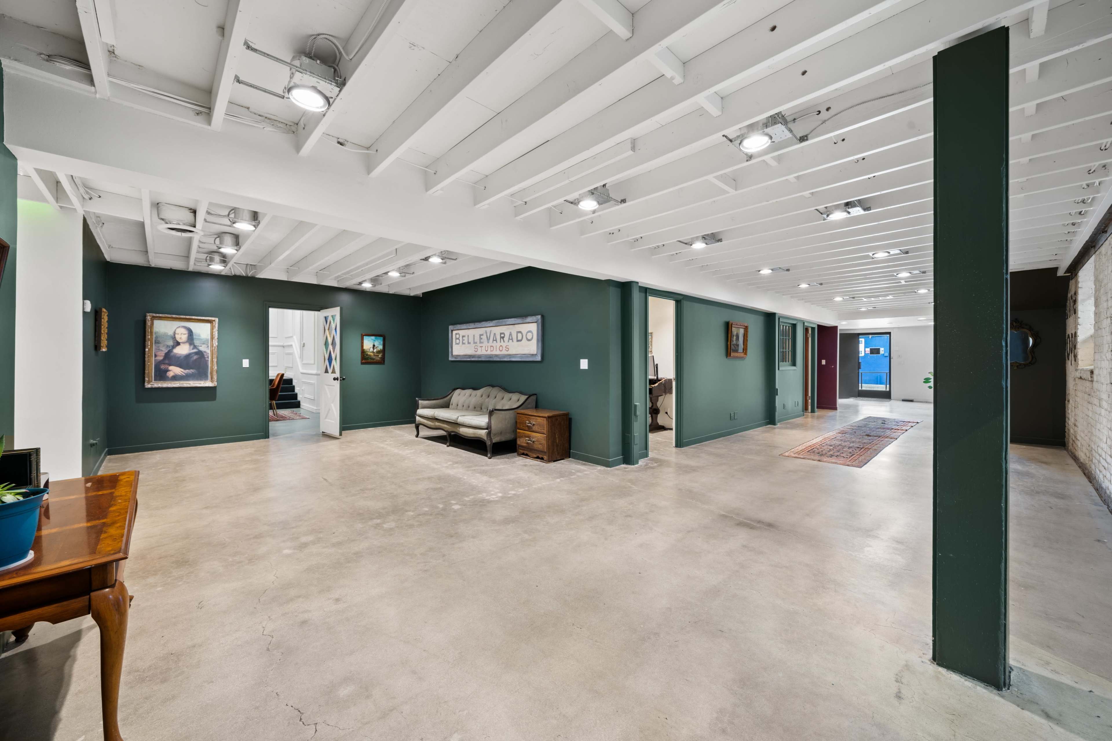 A spacious, well-lit interior area with green walls, exposed beams, and a mix of artwork and furniture.