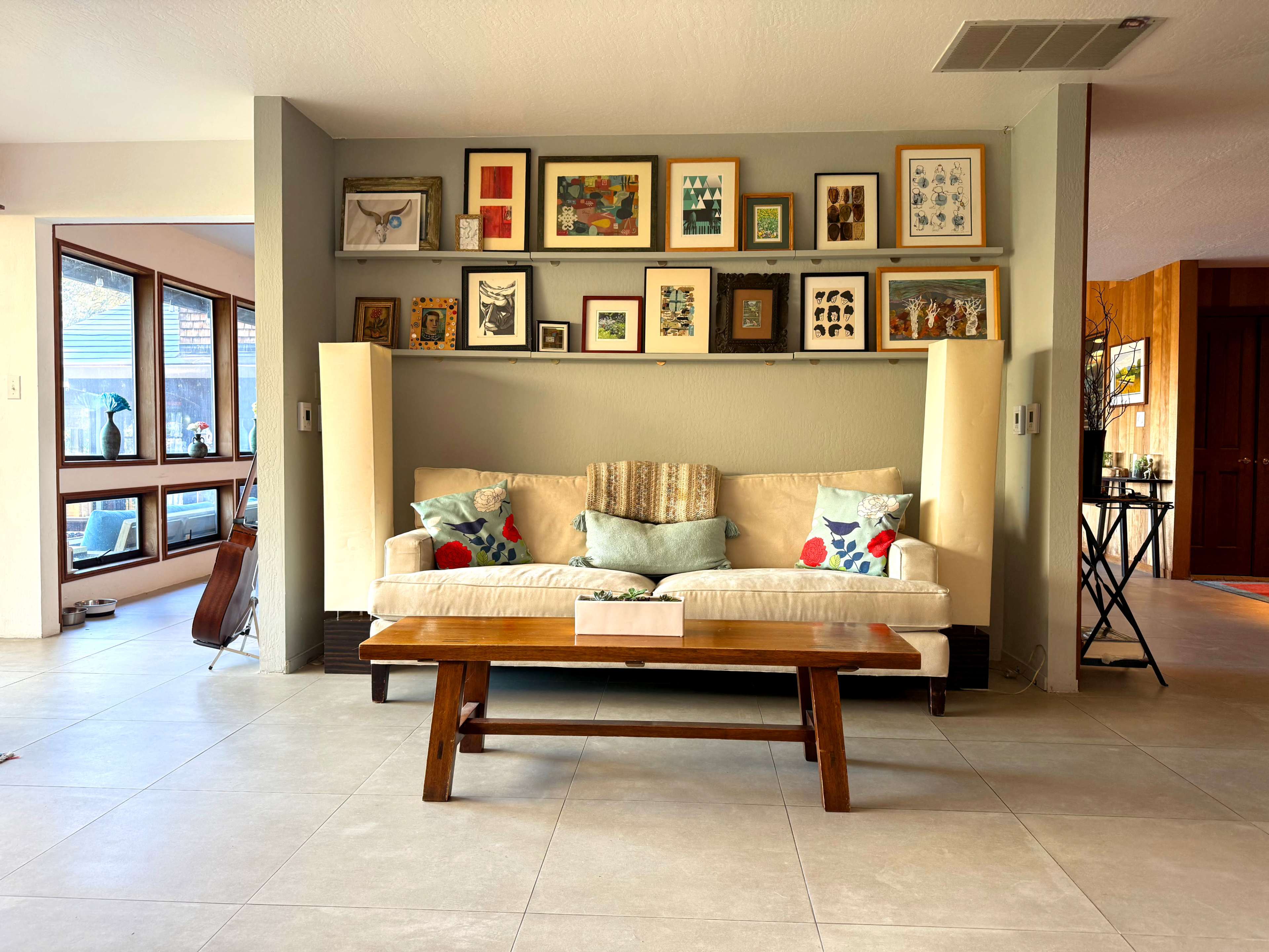 A beige sofa with decorative pillows is positioned in front of a wall displaying various framed artworks and photographs.