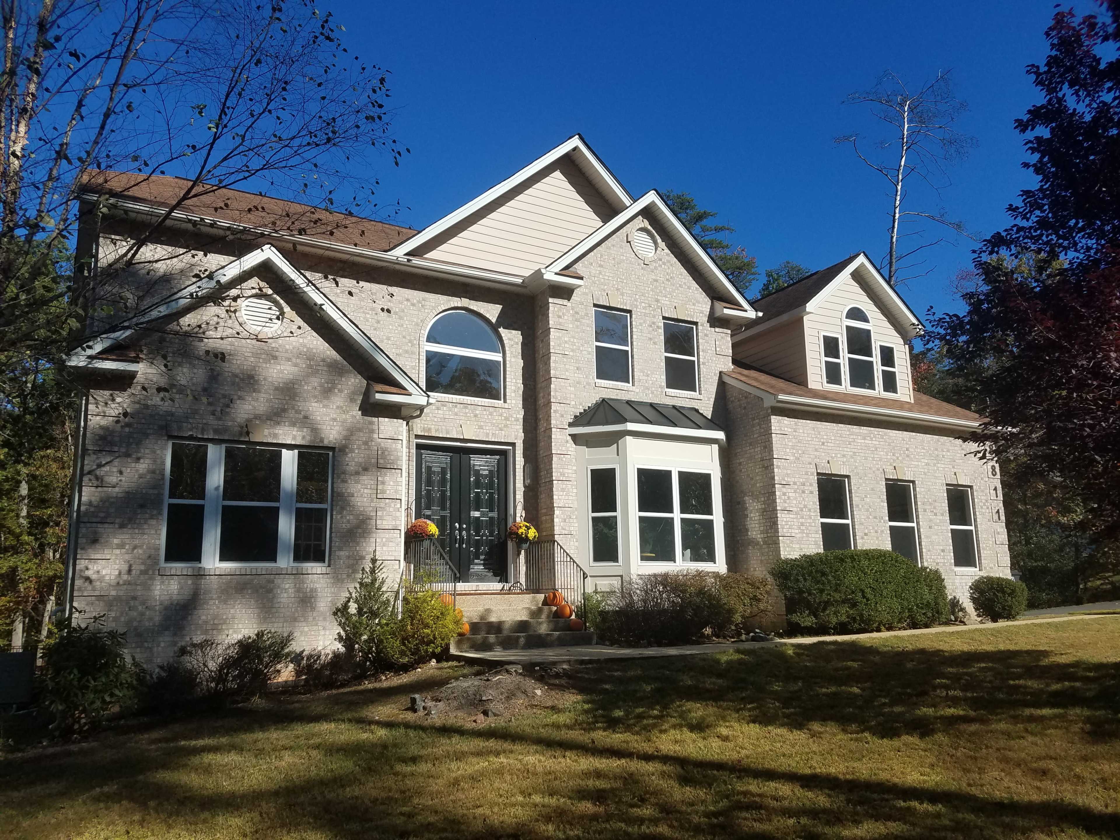 A two-story brick house features large windows, a peaked roof, and is surrounded by neatly maintained landscaping.