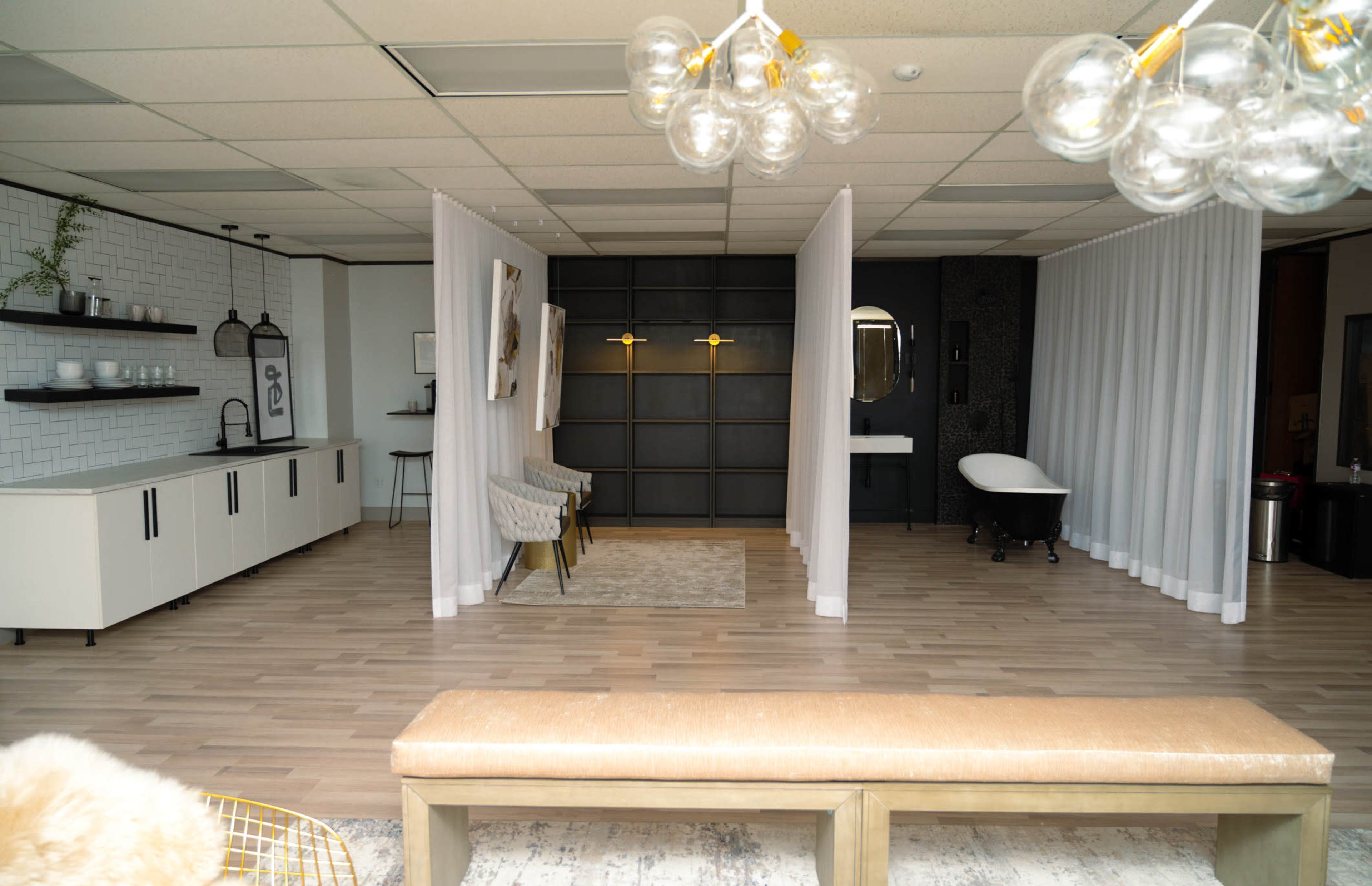 A modern interior of a spacious room with a minimalist design, featuring white curtains separating different areas, stylish seating, and a dramatic black accent wall with lighting.