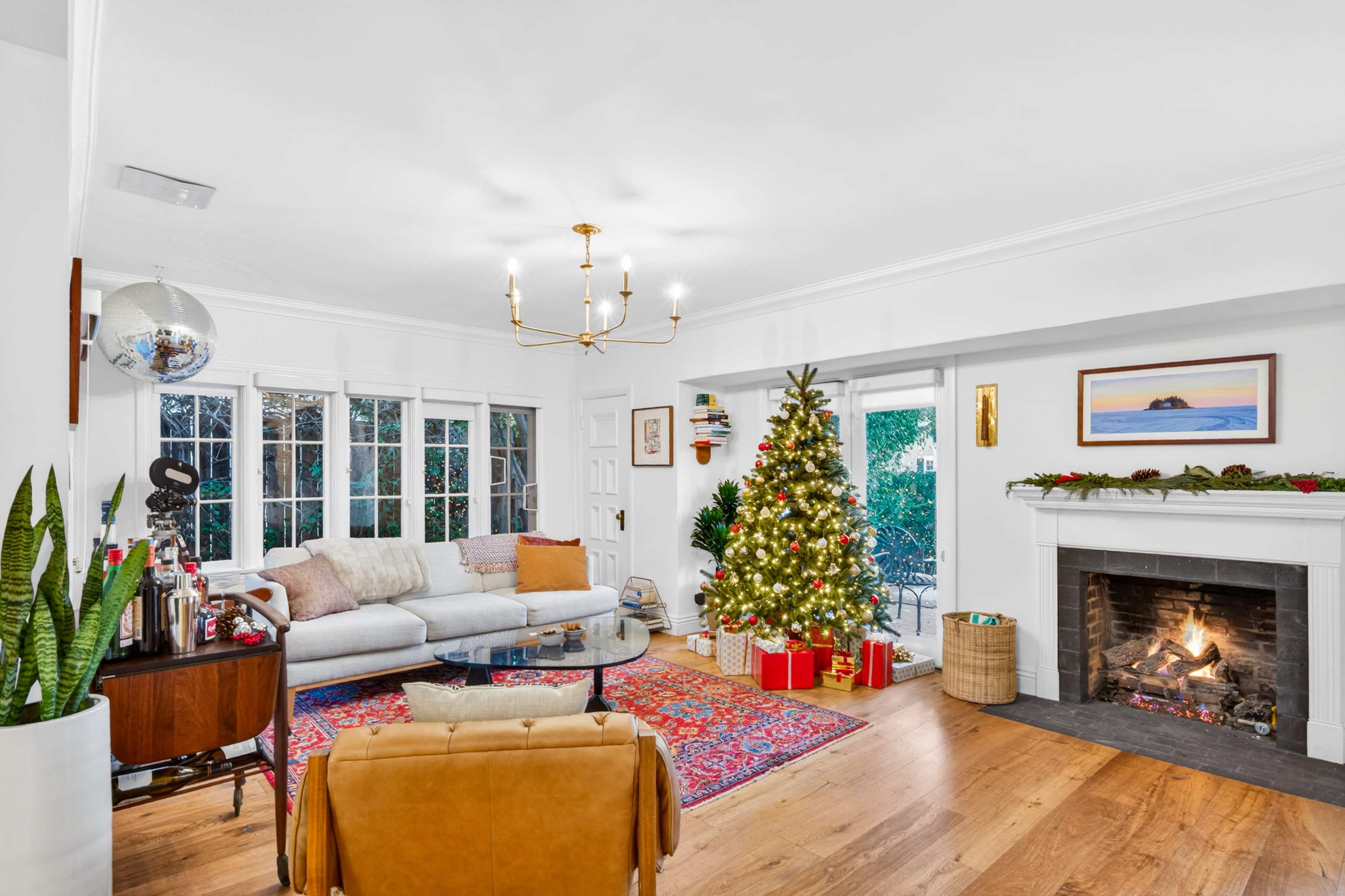 A cozy living room features a decorated Christmas tree, a festive fireplace, and a sectional sofa with an area rug.
