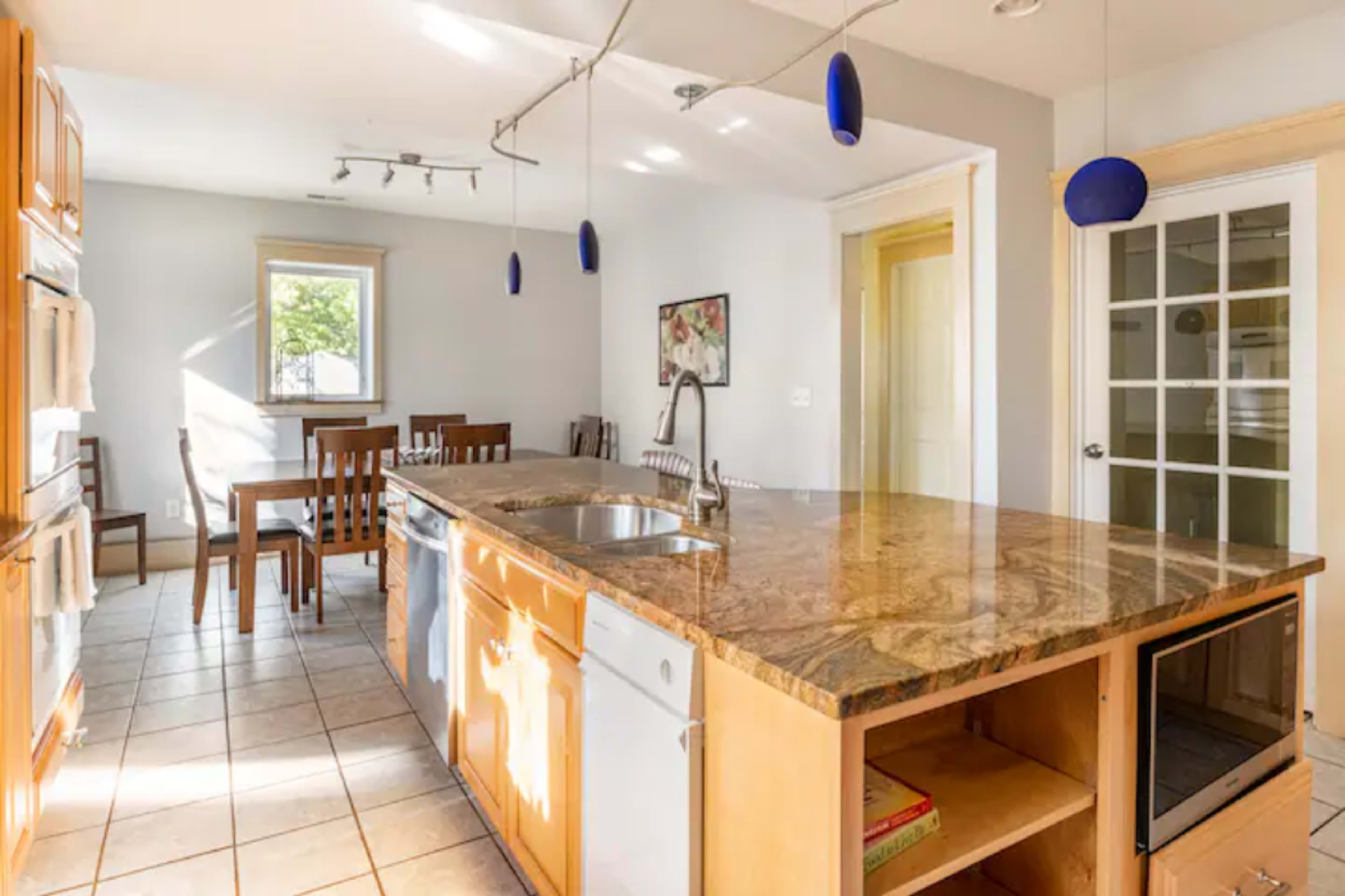 A kitchen features wooden cabinets, a granite countertop island with a sink, and a dining area with a table and chairs.