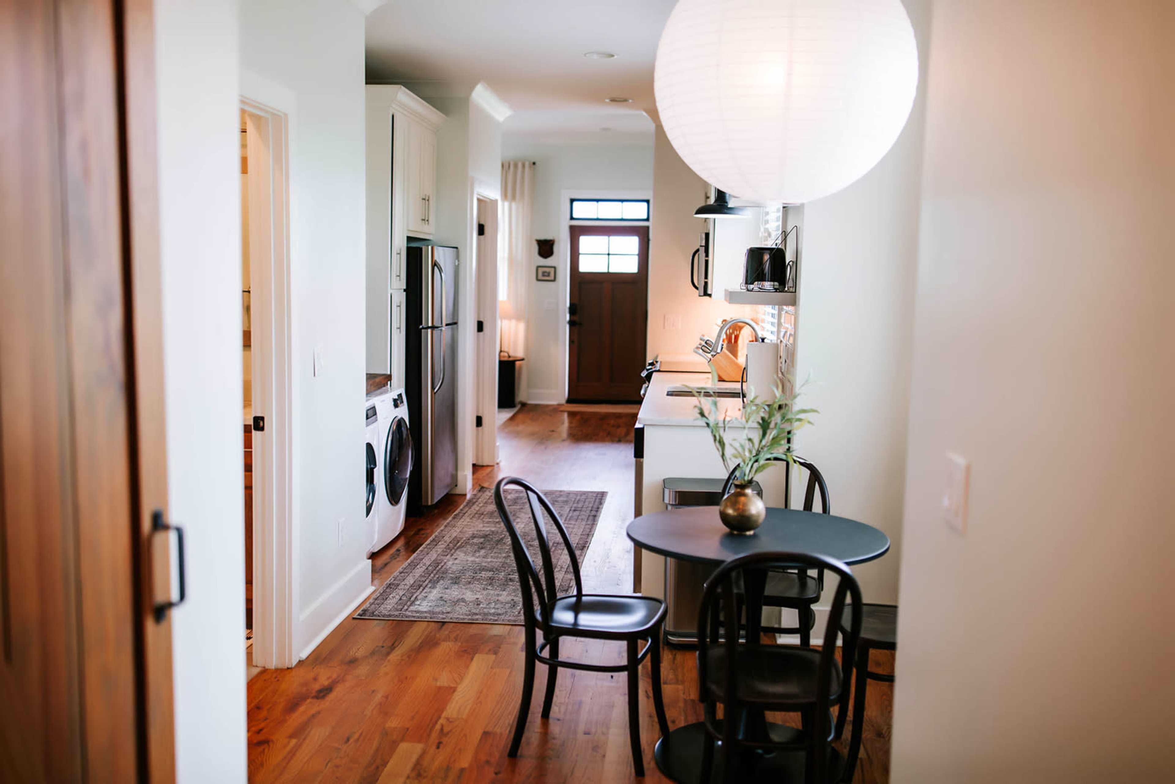 The image shows a narrow hallway leading to a kitchen area with a round dining table and chairs, along with laundry appliances in the adjacent space.