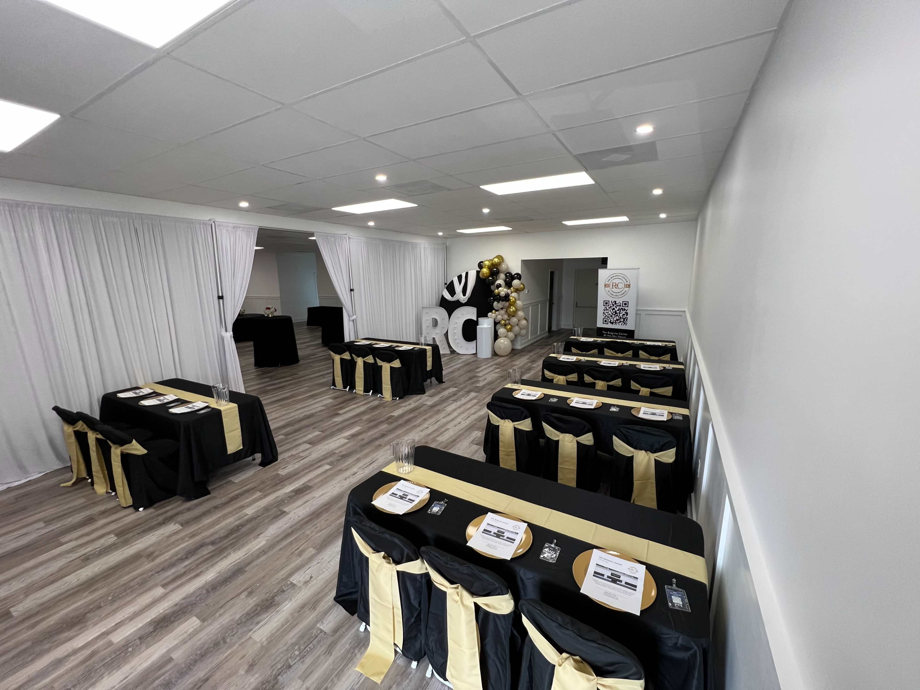 The room features multiple tables dressed in black and gold, arranged for an event, with decorative elements and a large "RCI" sign in the background.