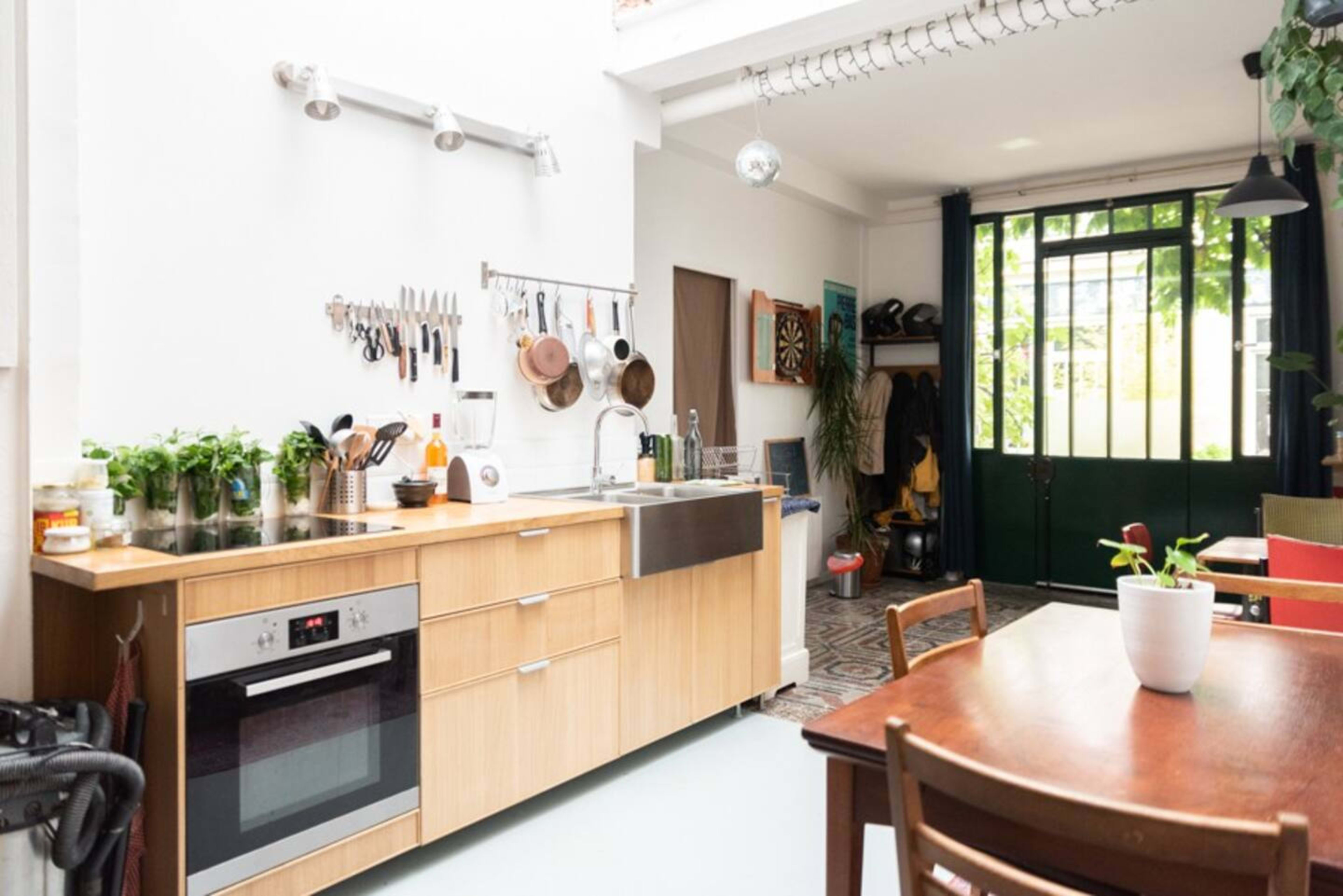 The image shows a modern kitchen with wooden cabinetry, a stainless steel sink, and a view of an outdoor area through a glass door.