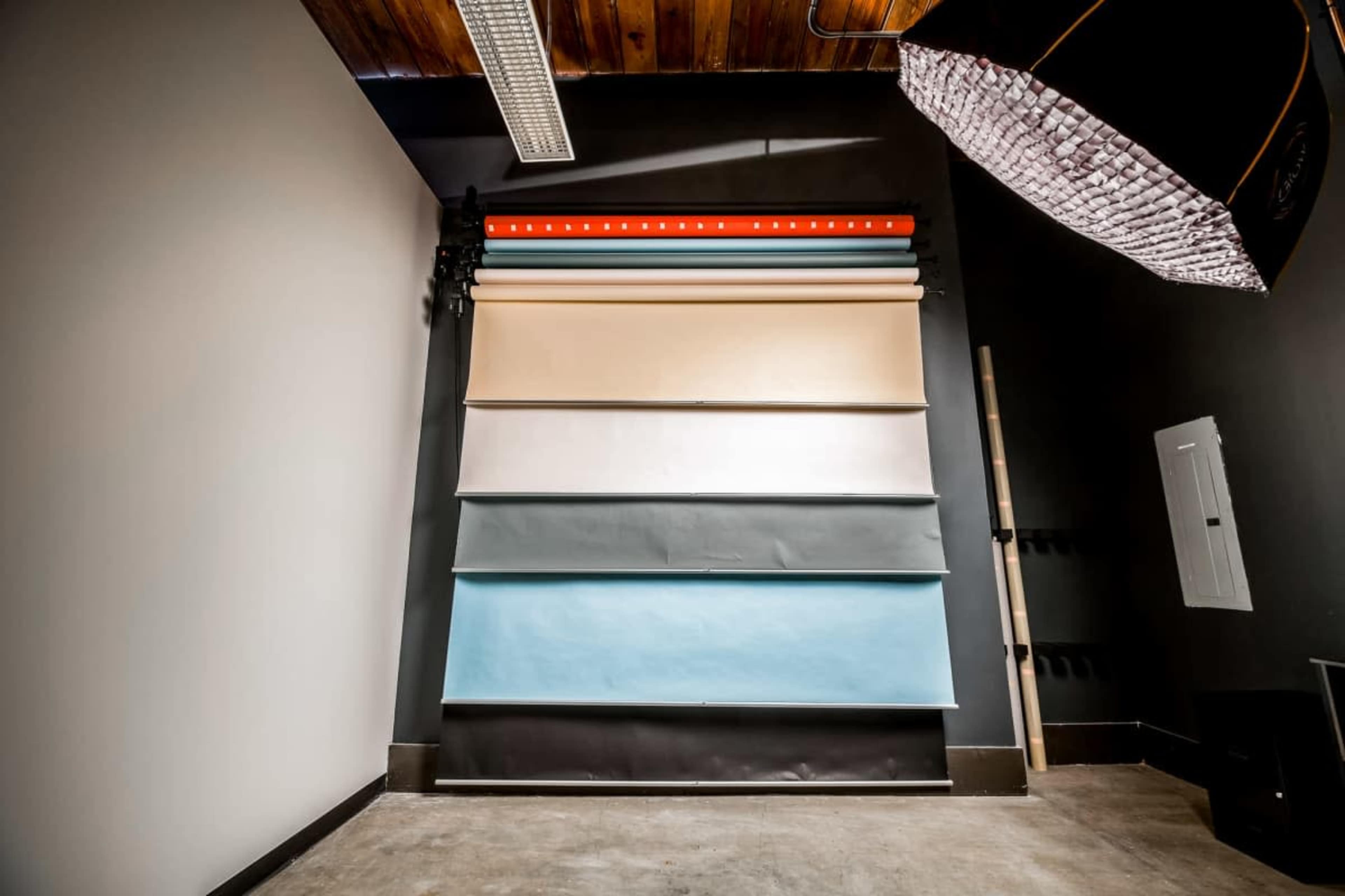 The image shows a photography backdrop setup featuring several rolls of different colored paper mounted on a wall, with softbox lighting positioned above.