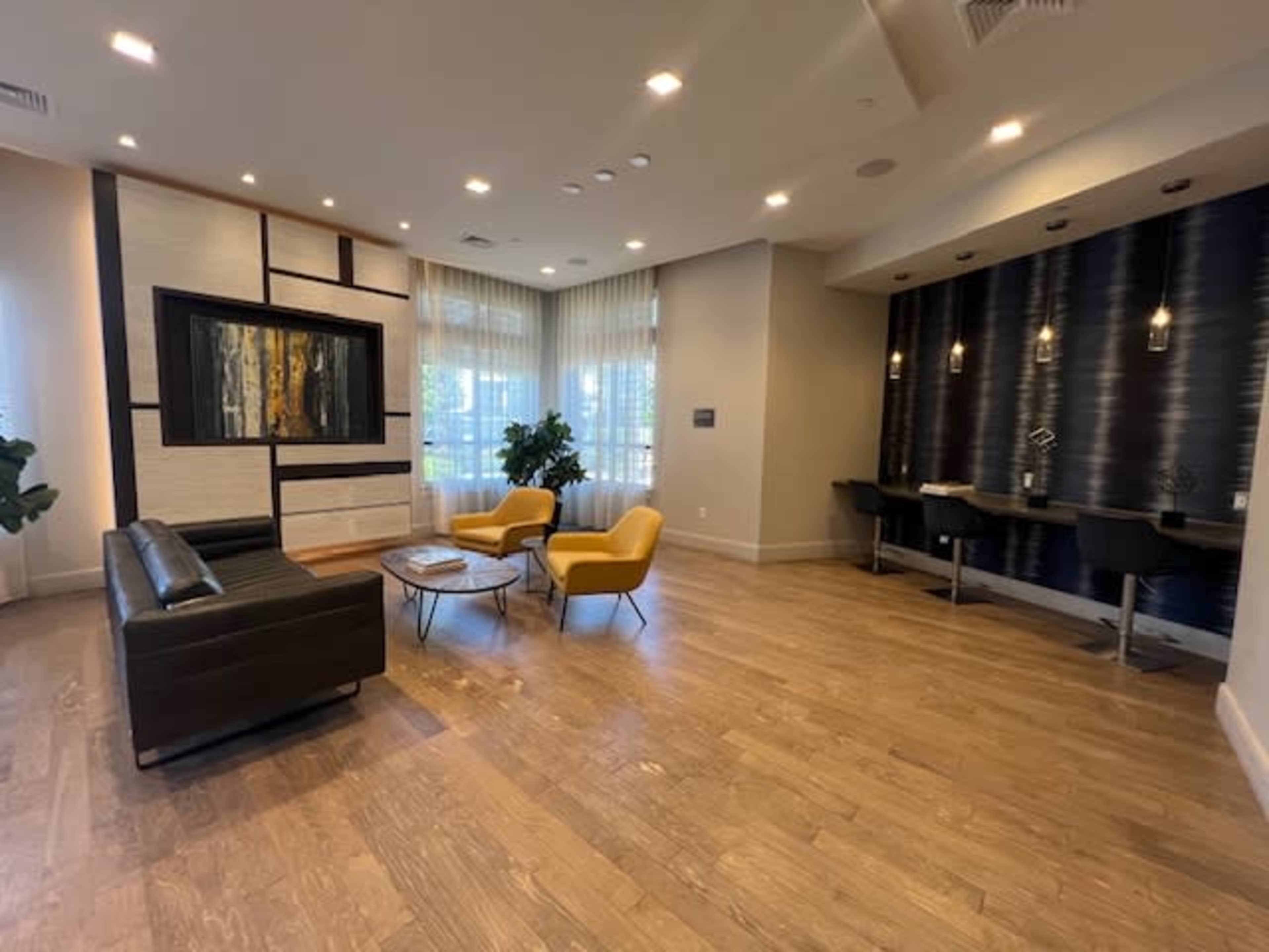 A modern living room with a black sofa, two yellow chairs, a round coffee table, and a small workspace against a textured wall.