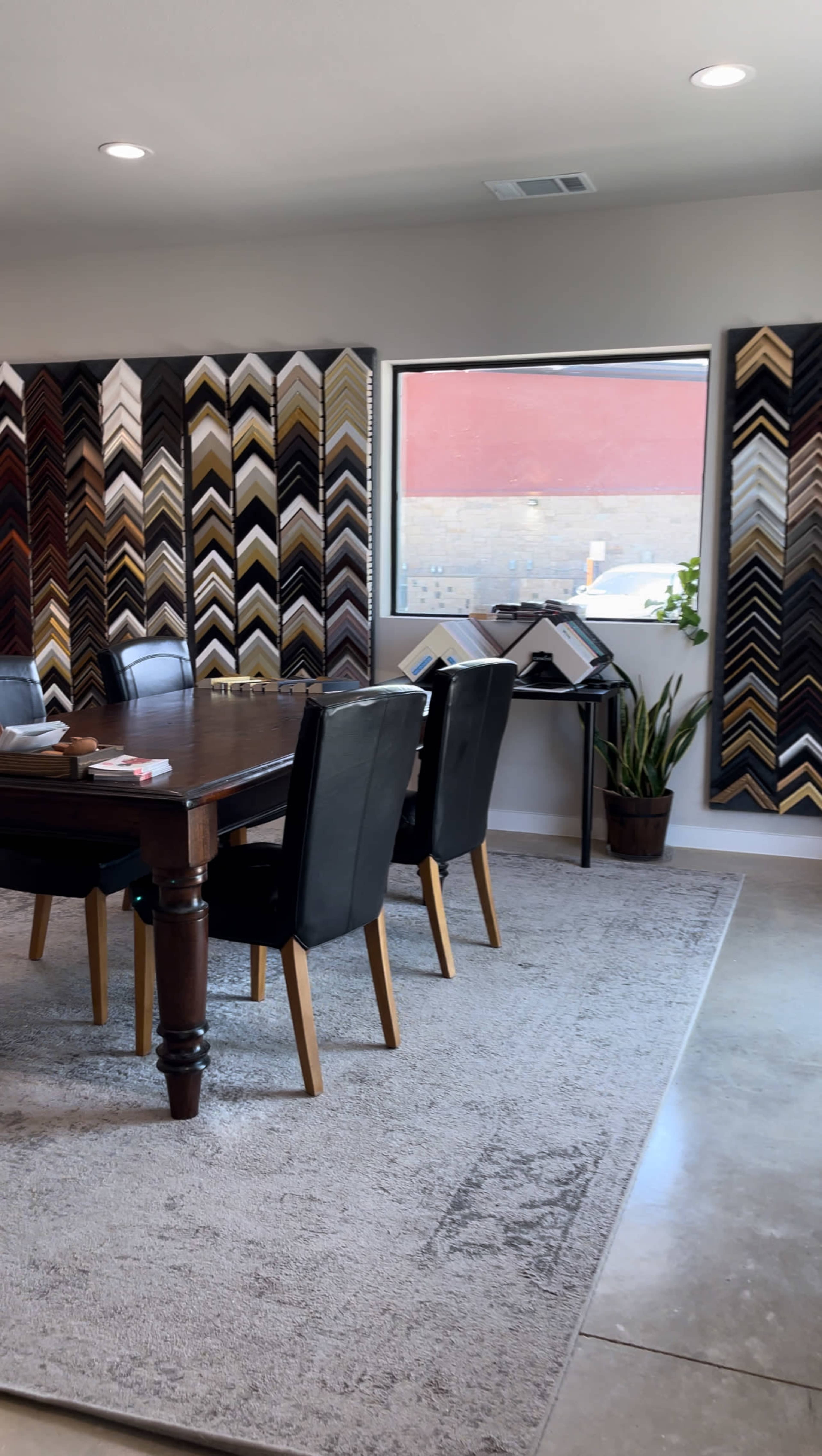 A dining area features a dark wooden table surrounded by black leather chairs, with a wall display of various picture frames in zigzag patterns.