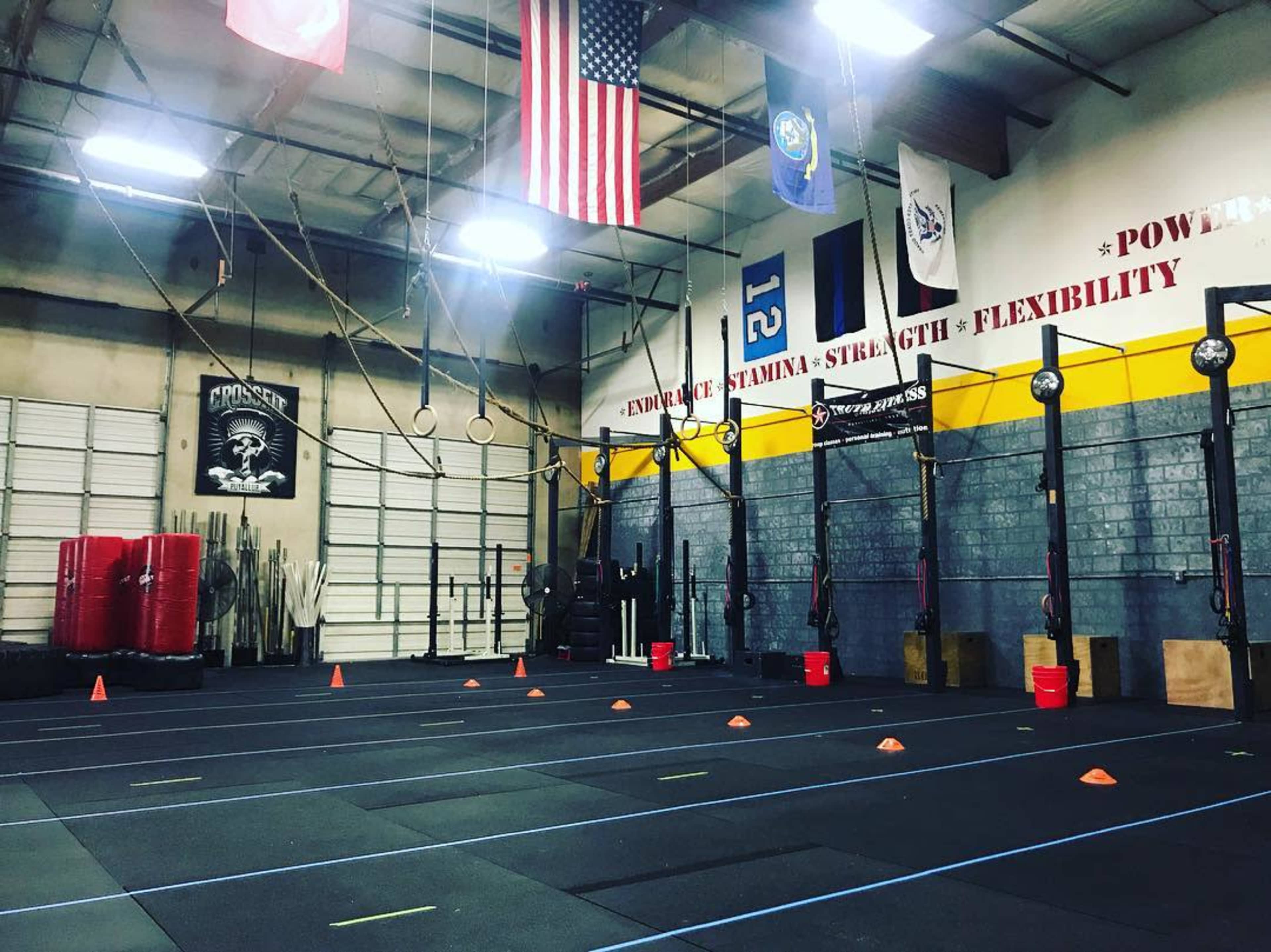 The image shows a gym interior with exercise mats, weightlifting equipment, and various training accessories such as cones and rings.