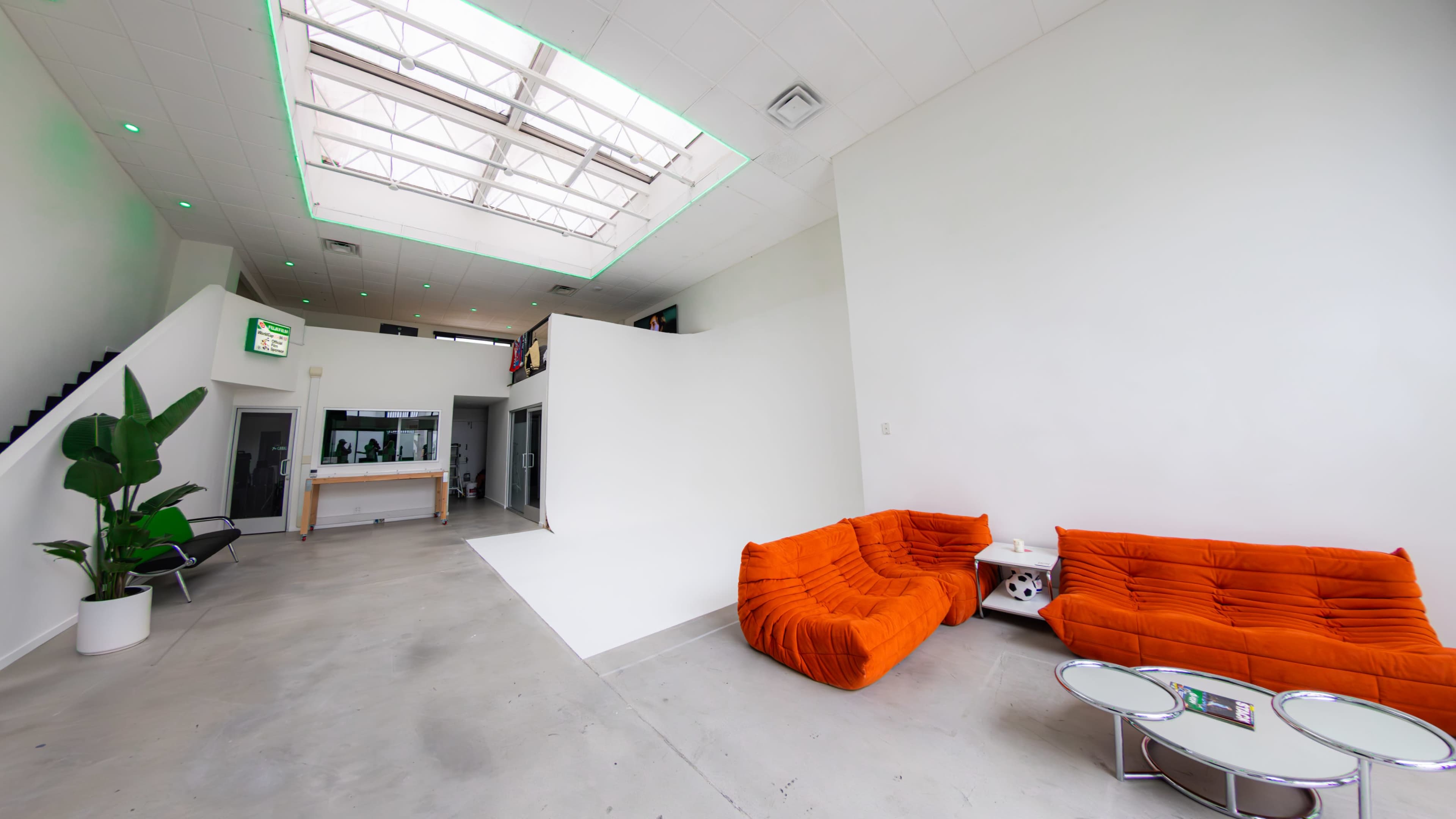 A modern interior with white walls, concrete flooring, orange sofas, and a skylight providing natural light.