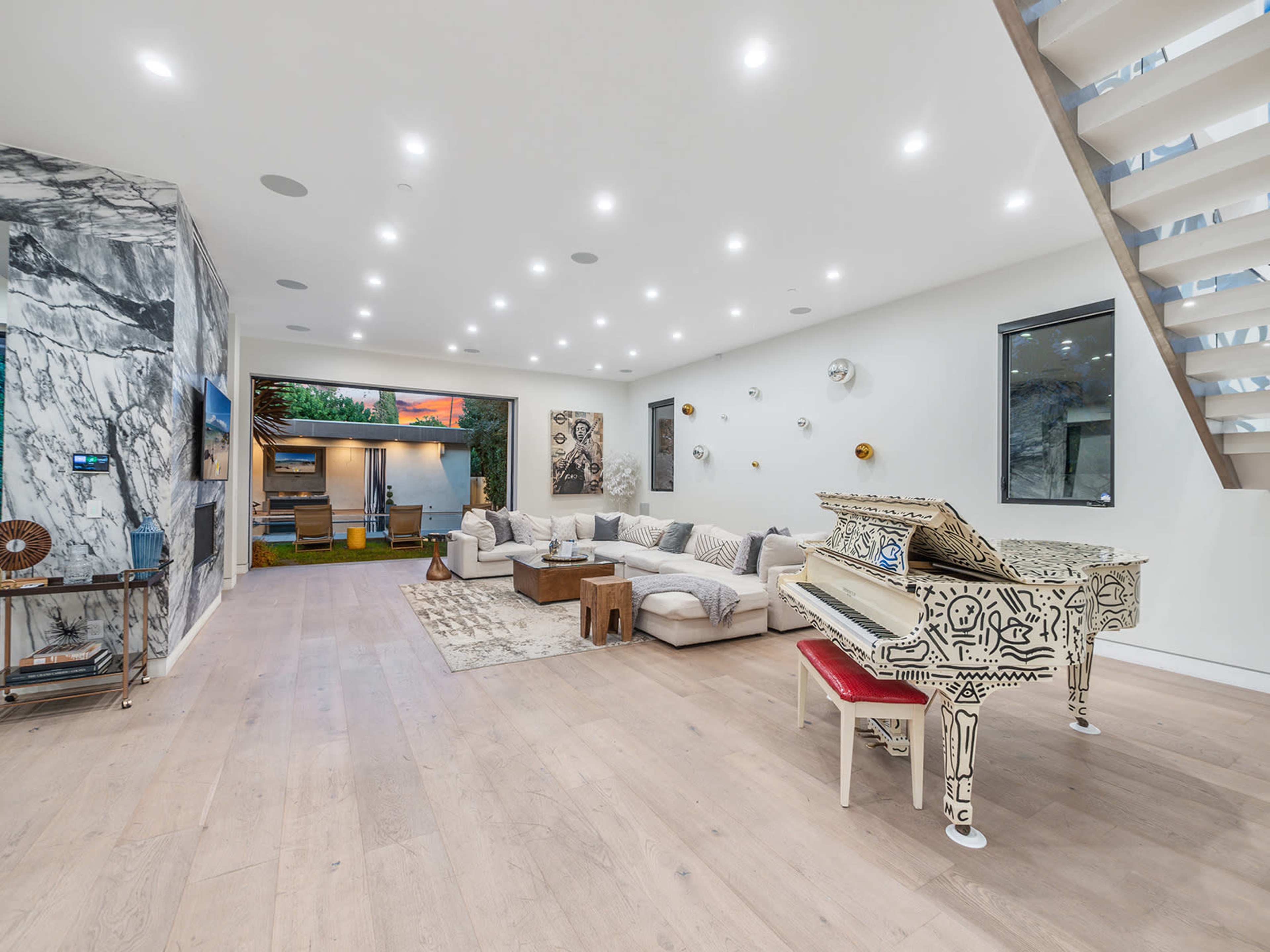 A spacious living room with a patterned piano, a large sectional sofa, and artwork on the walls, illuminated by ceiling lights.