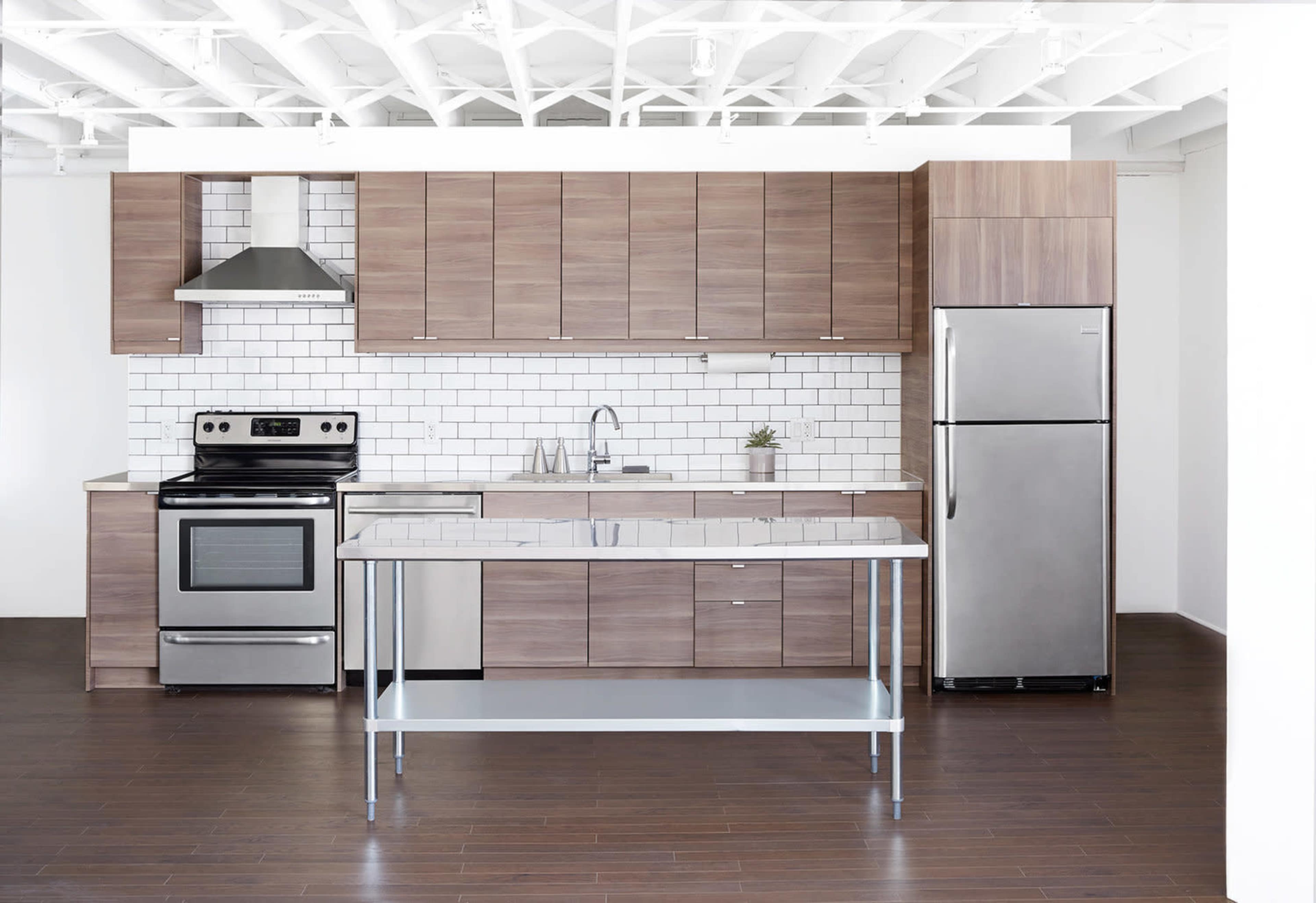 A modern kitchen with wooden cabinets, stainless steel appliances, and a central island on a dark wood floor.