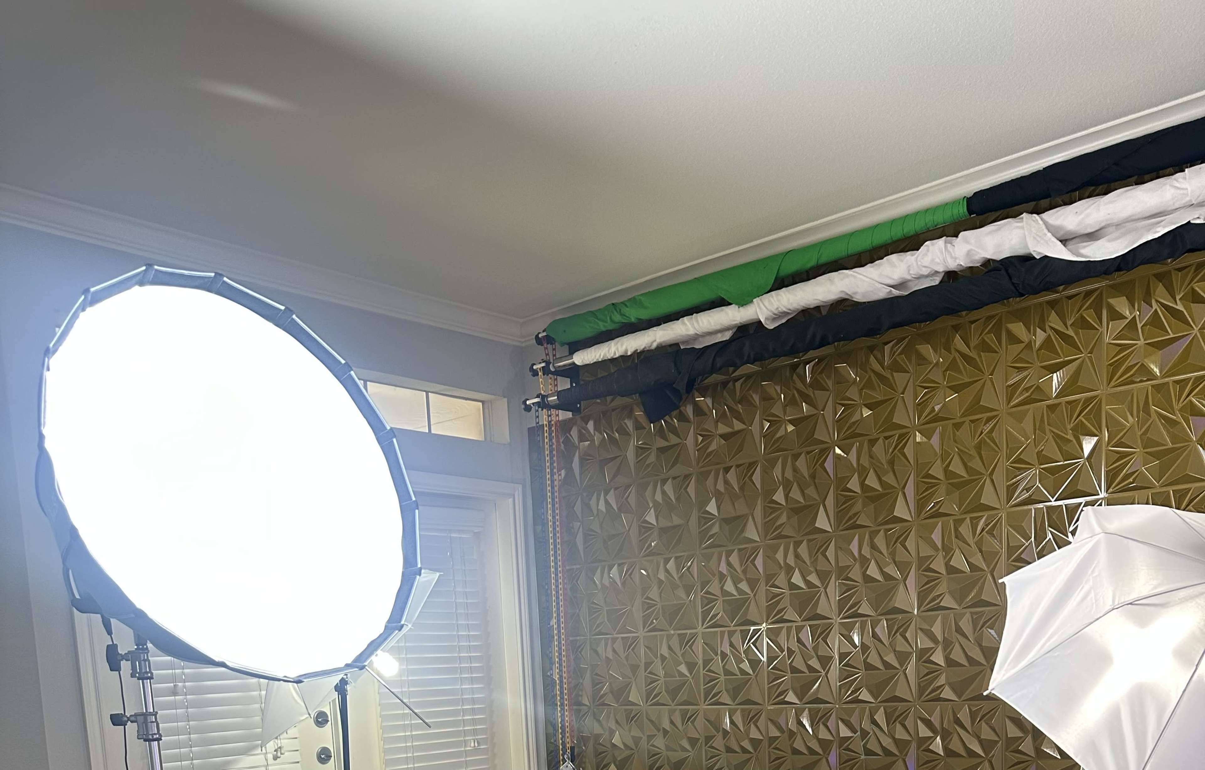 The image shows a room with a large light source and a textured gold wall with fabric drapes arranged above it.