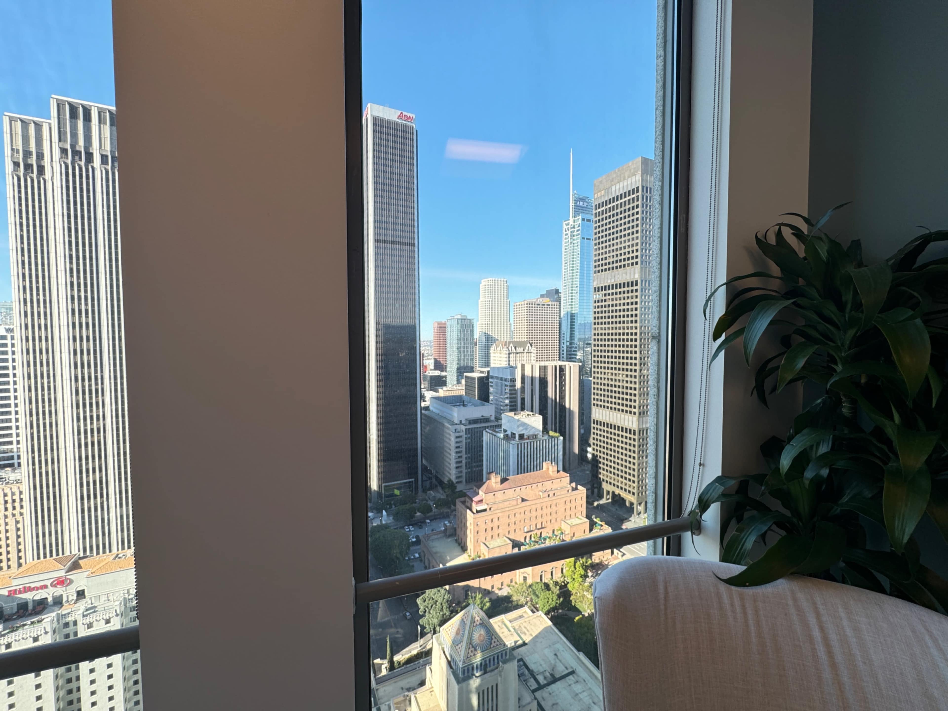 The image shows a city skyline view from an office window, featuring various high-rise buildings under a clear blue sky.