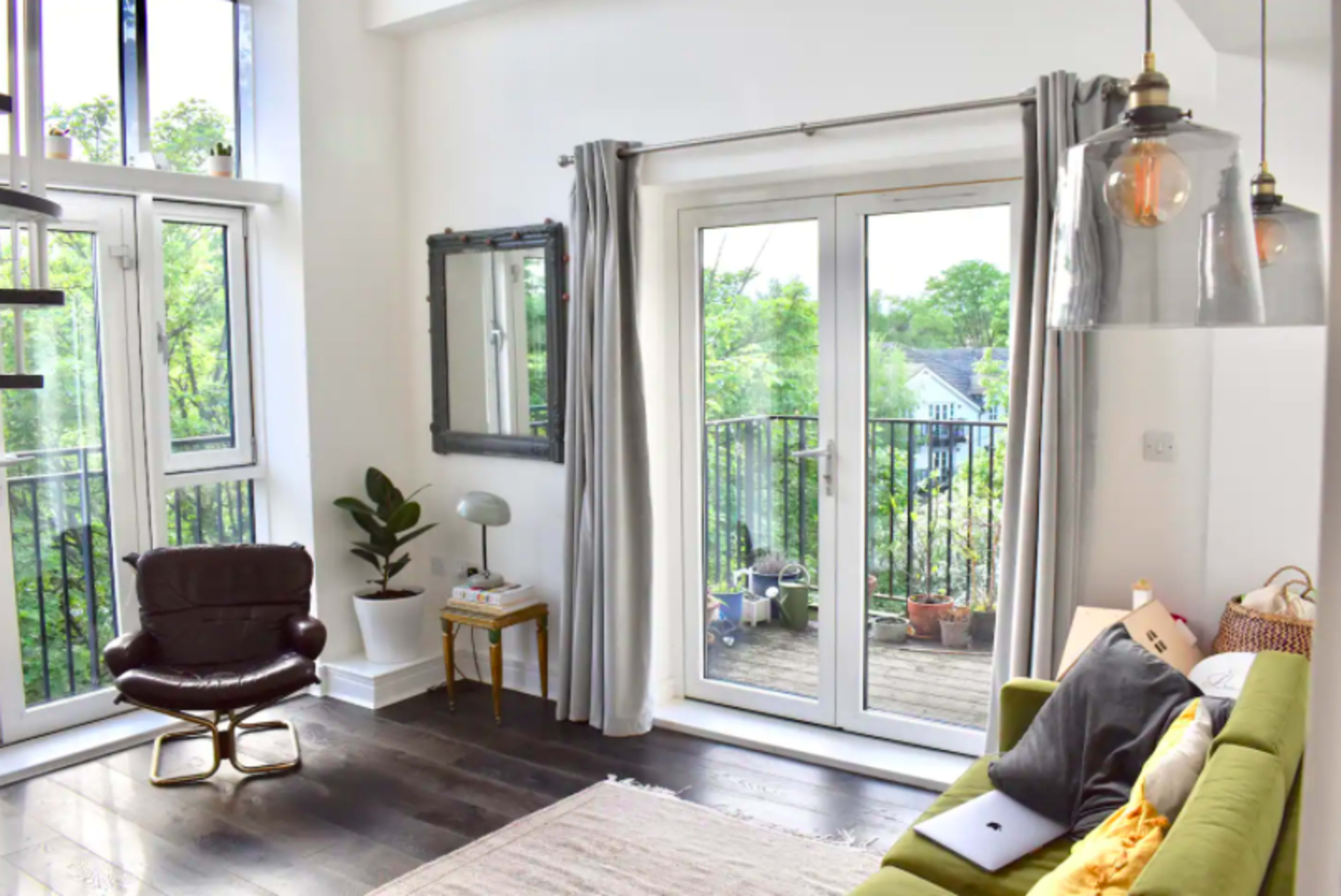 A living room features a green sofa, a brown chair, and large glass doors leading to a balcony surrounded by greenery.