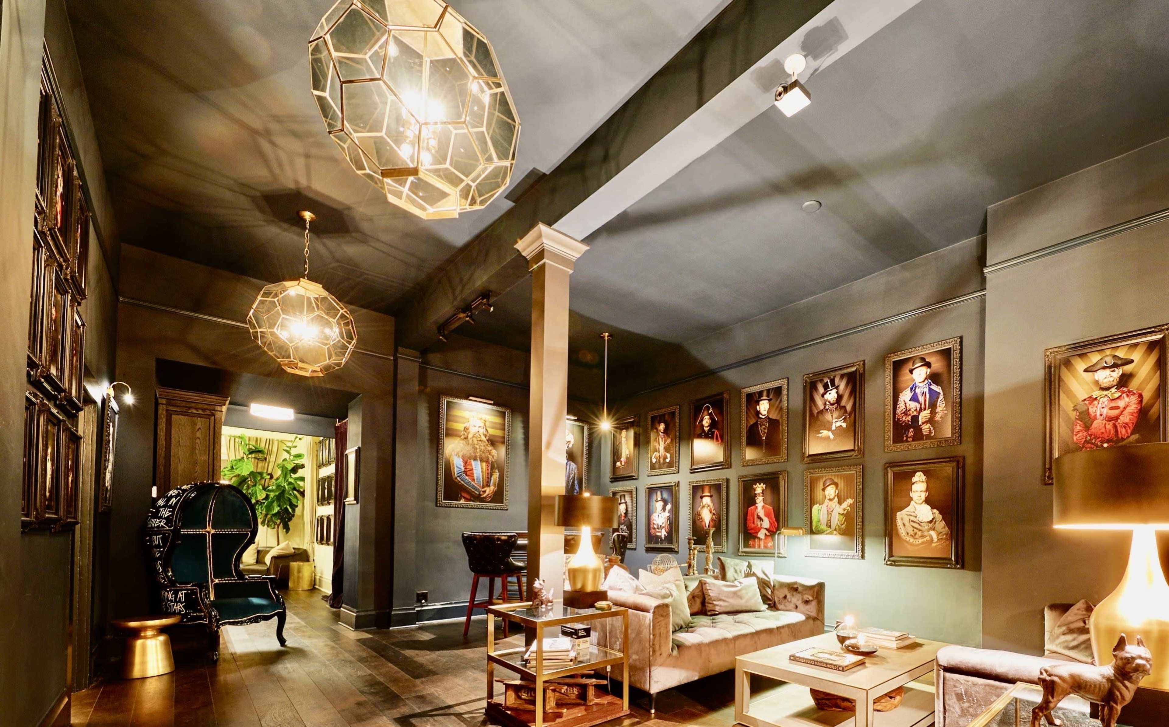 A modern living room with dark walls, featuring framed portraits on the walls, stylish lighting fixtures, and contemporary furniture.