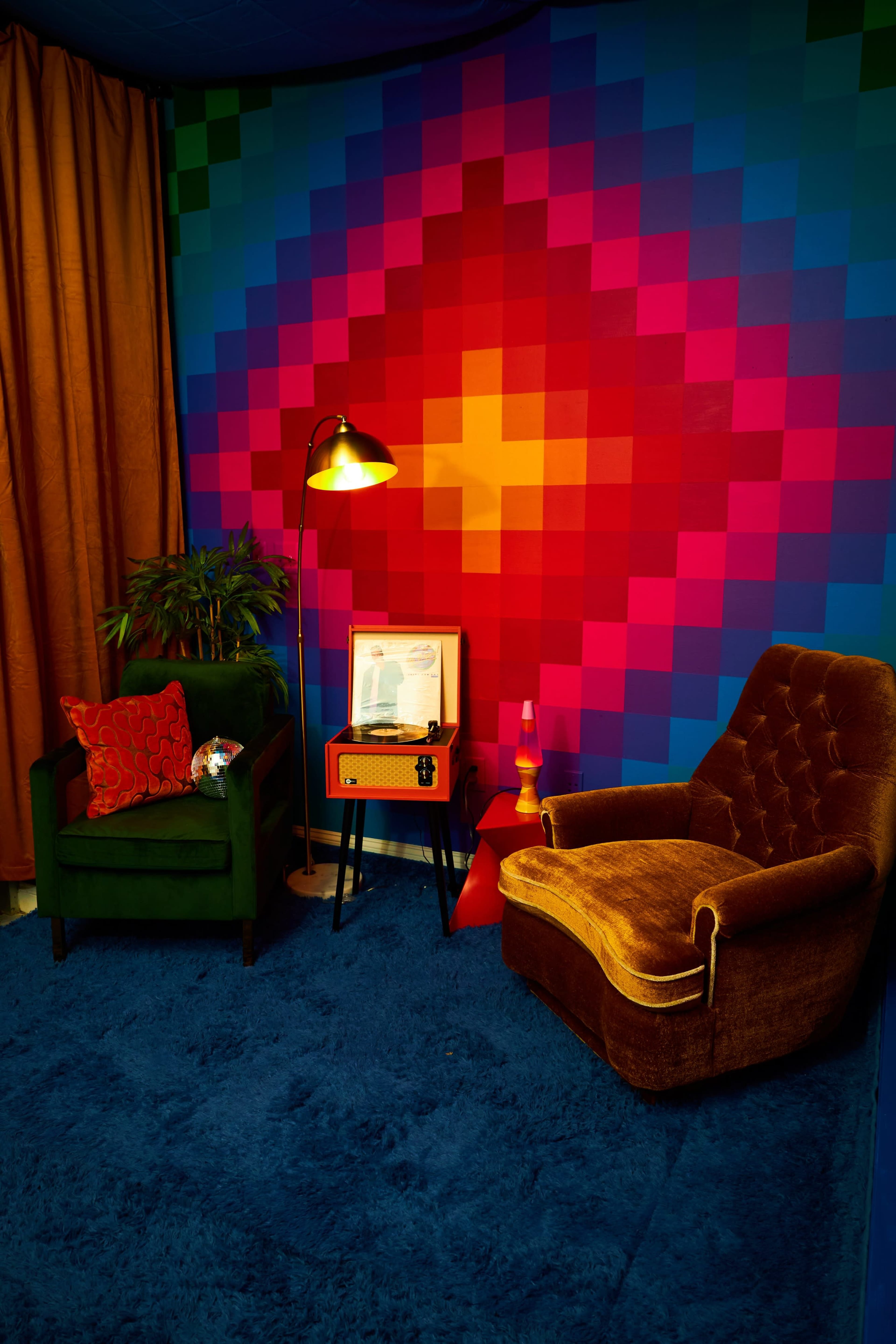 A colorful living space featuring two chairs, a lamp, a coffee table, and a patterned wall with vibrant squares.