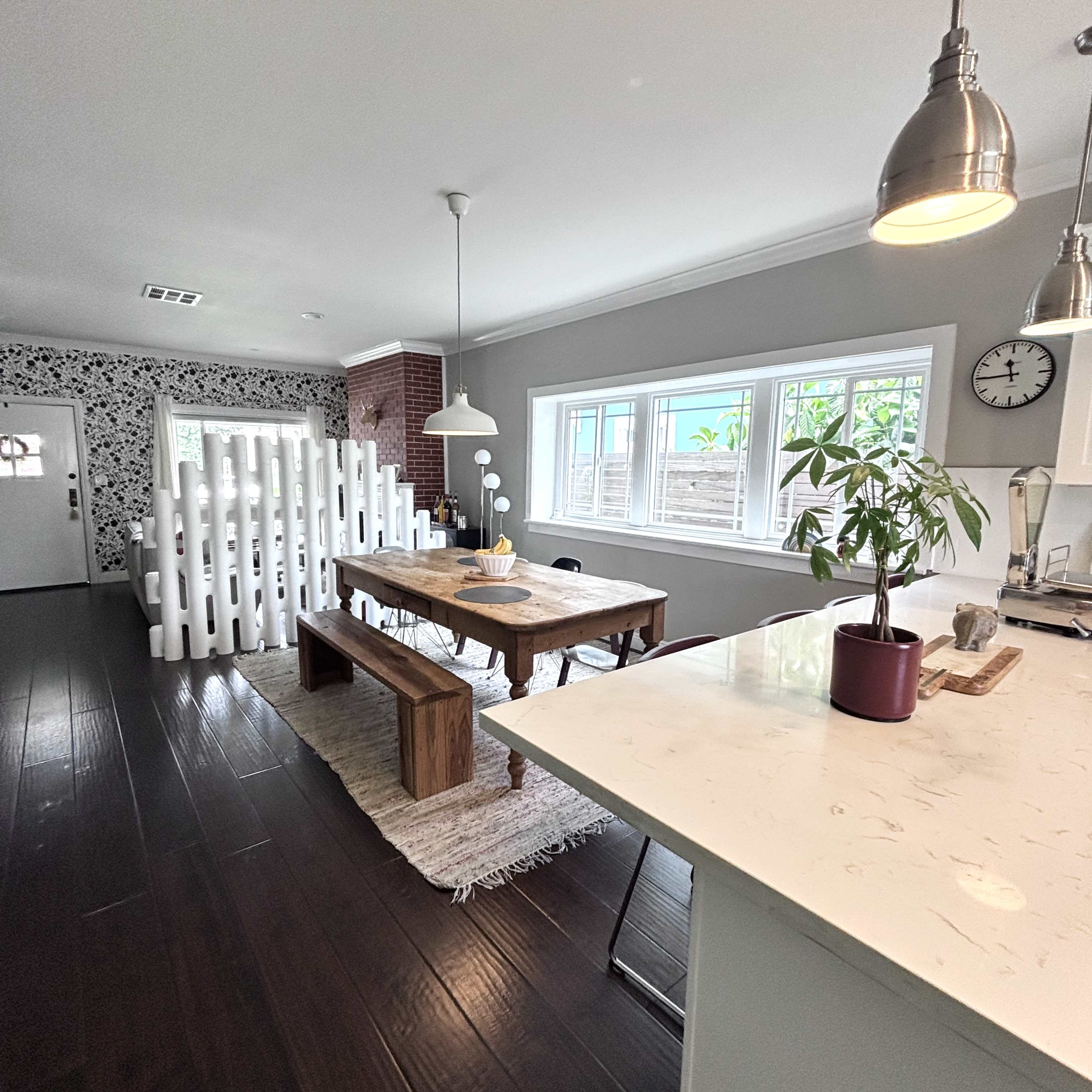 A modern dining area features a wooden table with benches, a decorative partition, and large windows that allow natural light to illuminate the space.