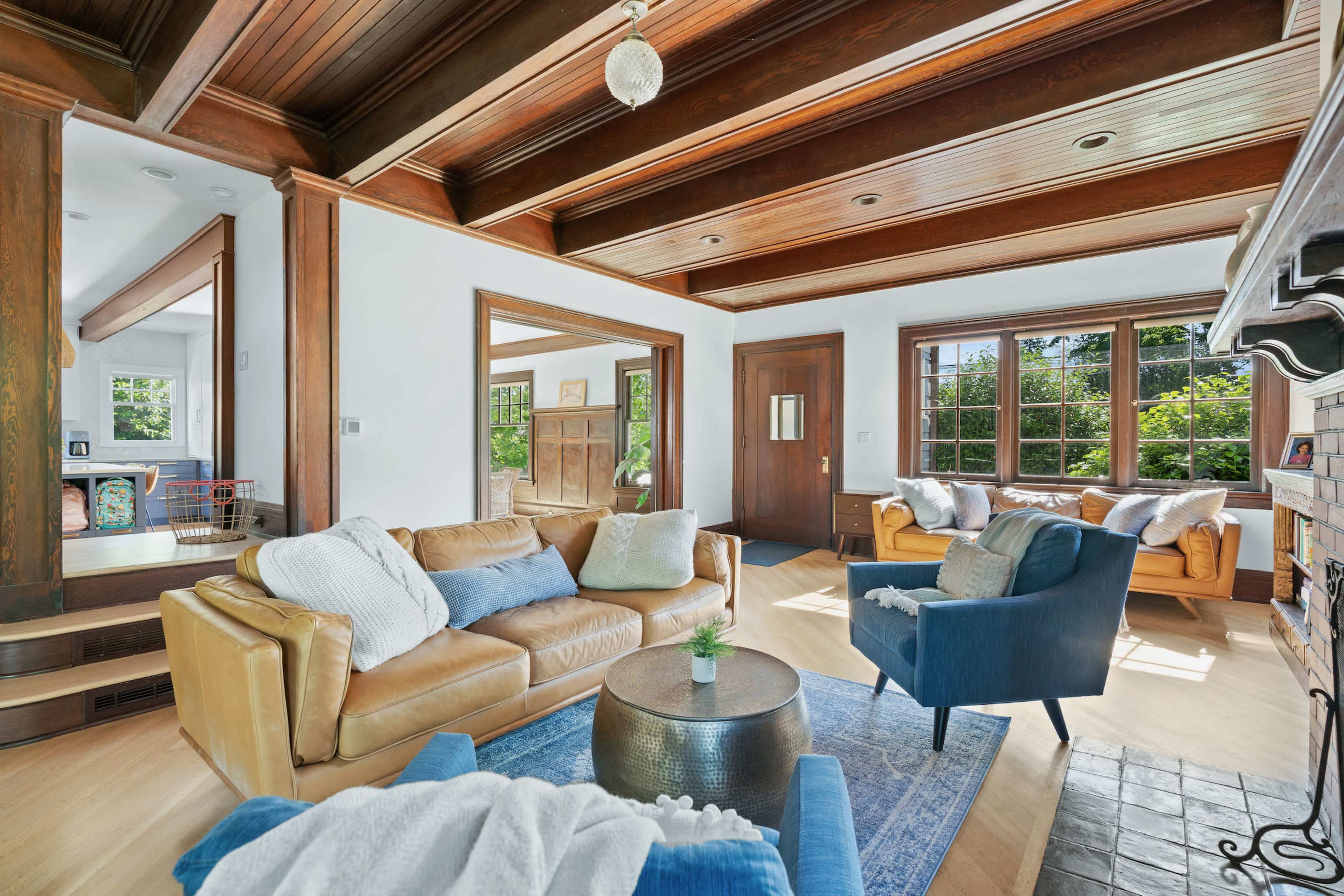 The living room features a mix of seating options, including a brown leather sofa and blue armchairs, with large windows allowing natural light to fill the space.