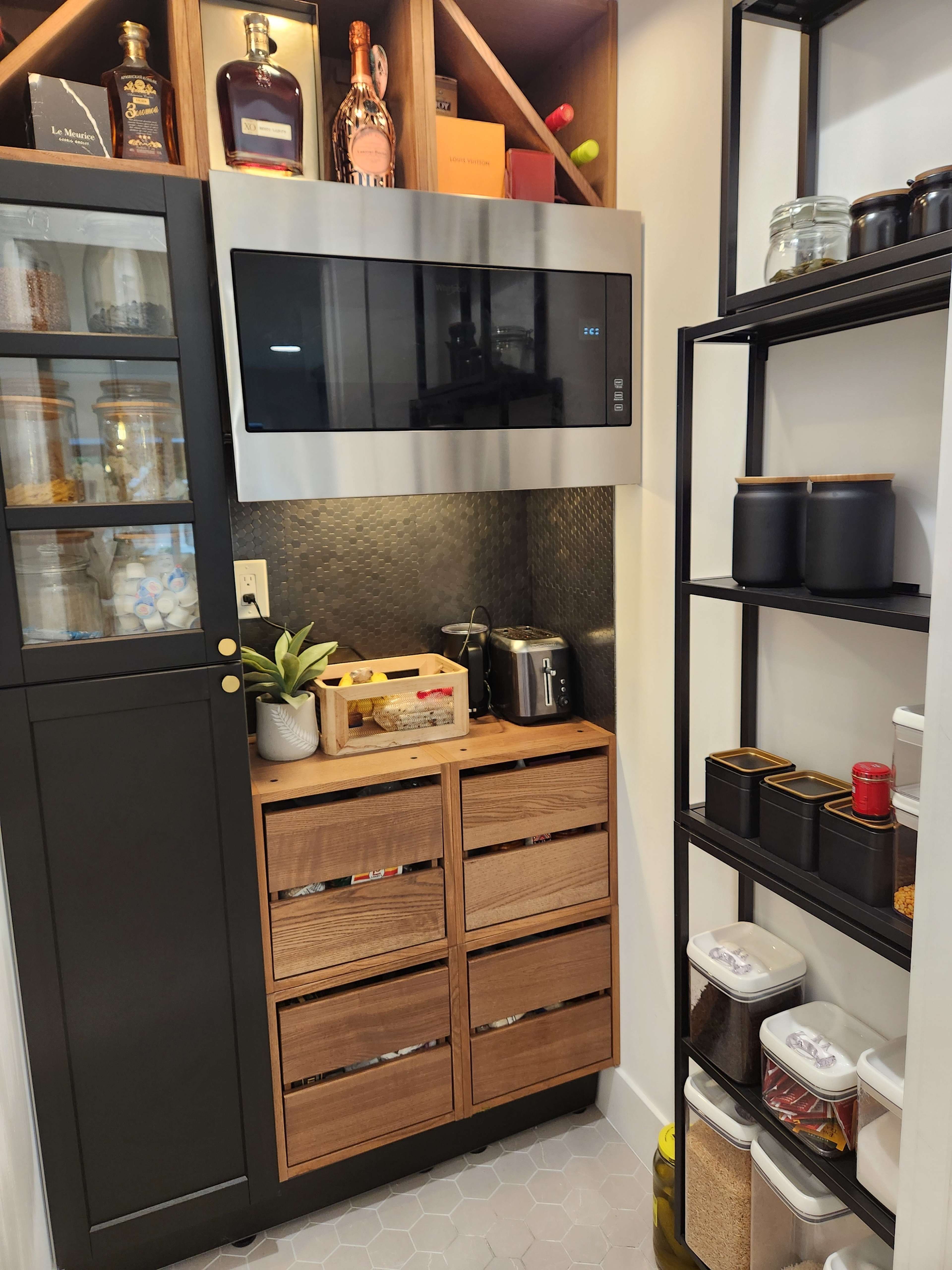 A compact kitchen pantry featuring a microwave, wooden storage drawers, and neatly organized shelves with glass and plastic containers.