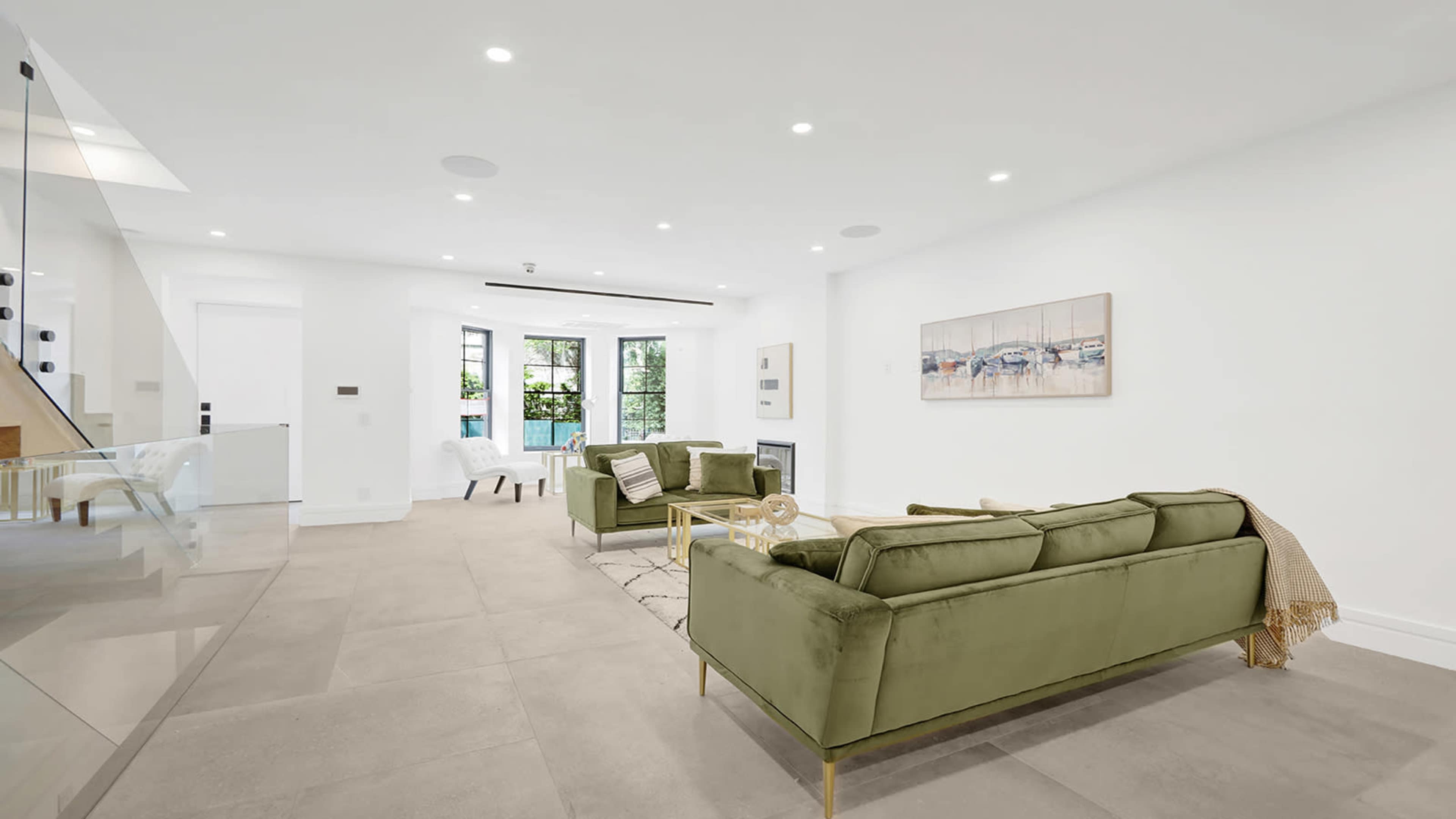 A modern living room with two green sofas, a coffee table, and large windows letting in natural light.