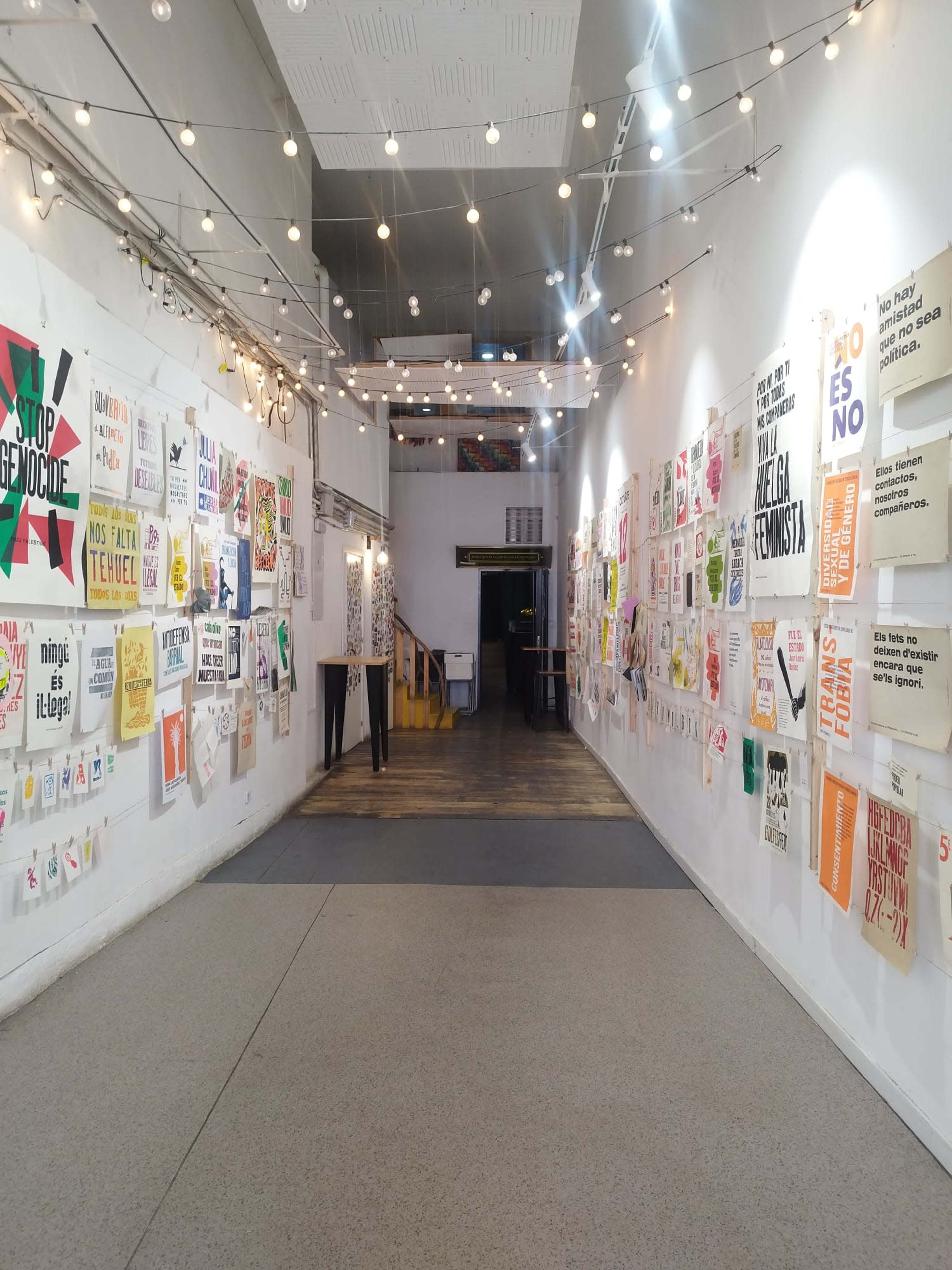 The image shows a spacious hallway adorned with various posters and art pieces on the walls, leading to an open area at the end.