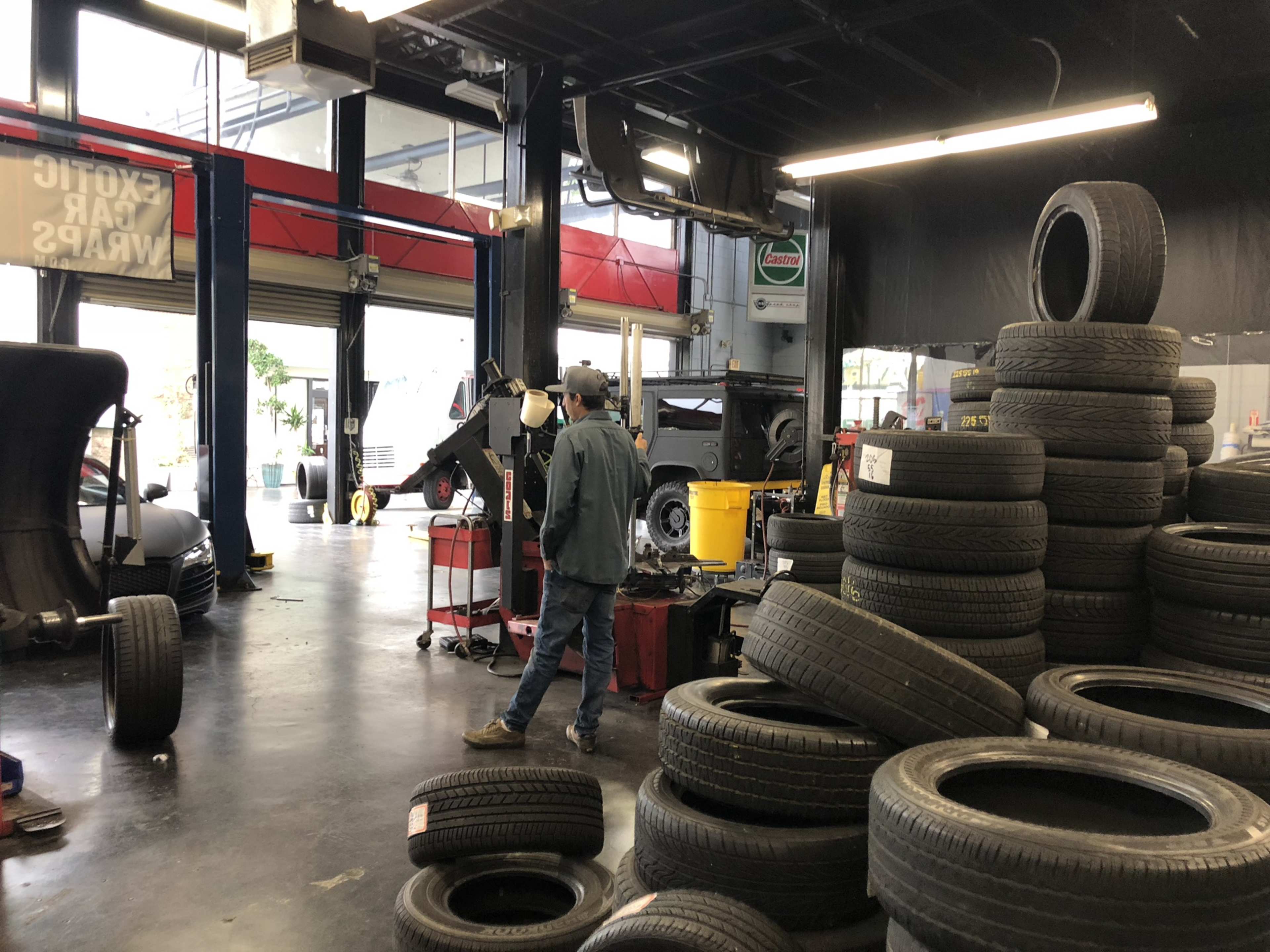 A mechanic walks past a stack of used tires in a bustling auto repair shop.