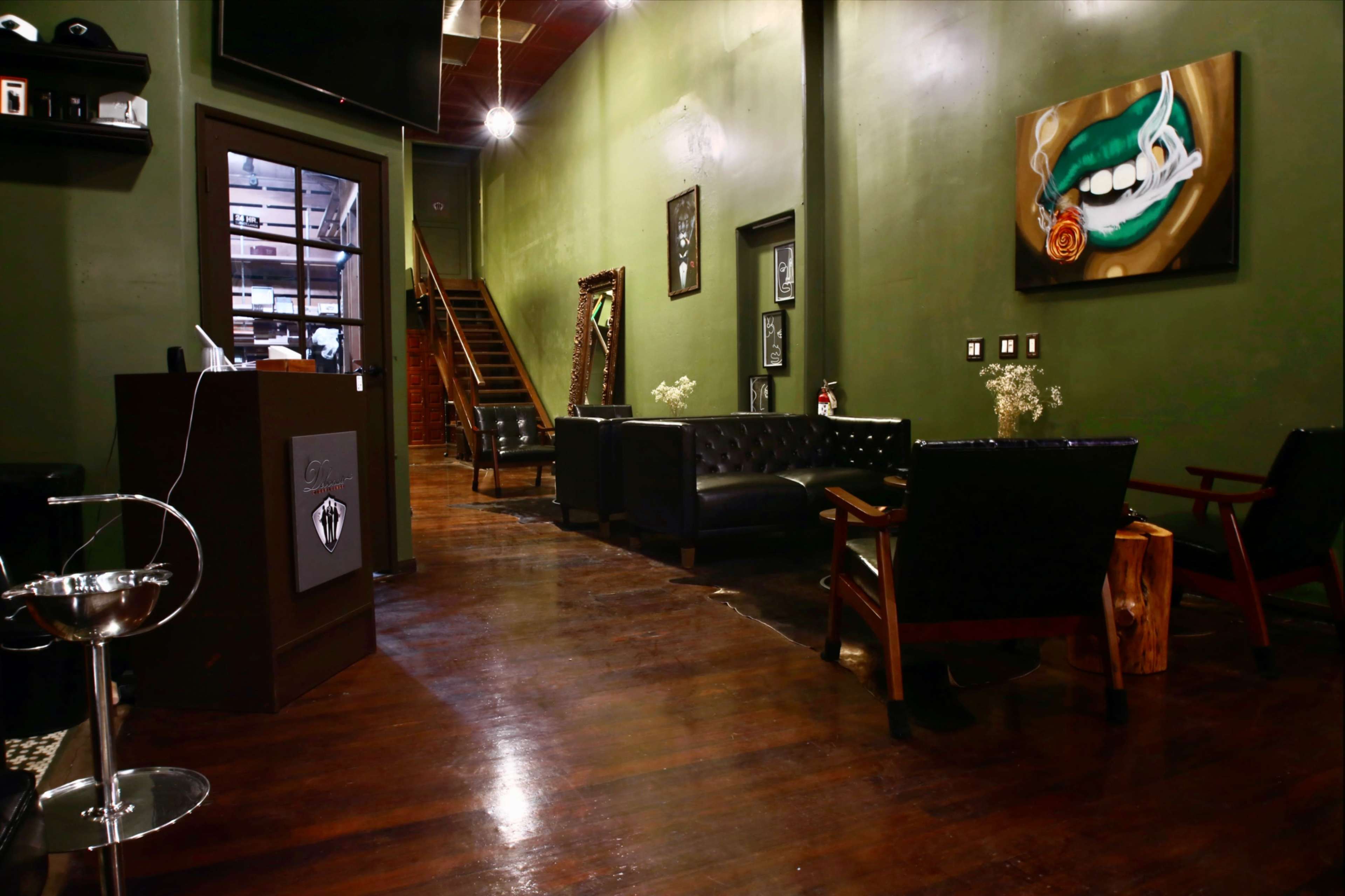 The image shows a dimly lit waiting area with dark wooden floors, green walls, and black leather seating, leading to a staircase in the background.