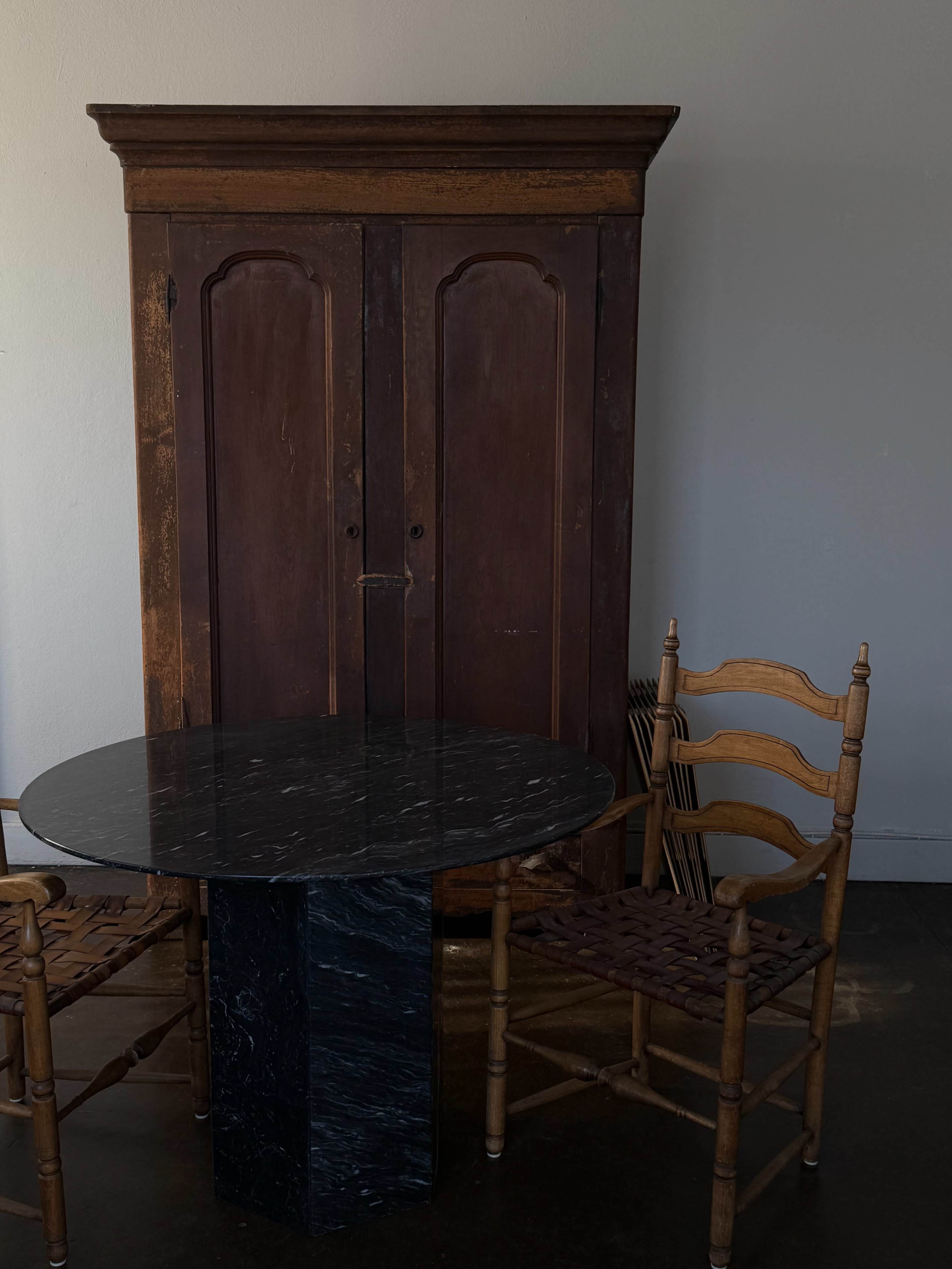 A wooden cabinet stands next to a round black marble table with two woven chairs on either side.
