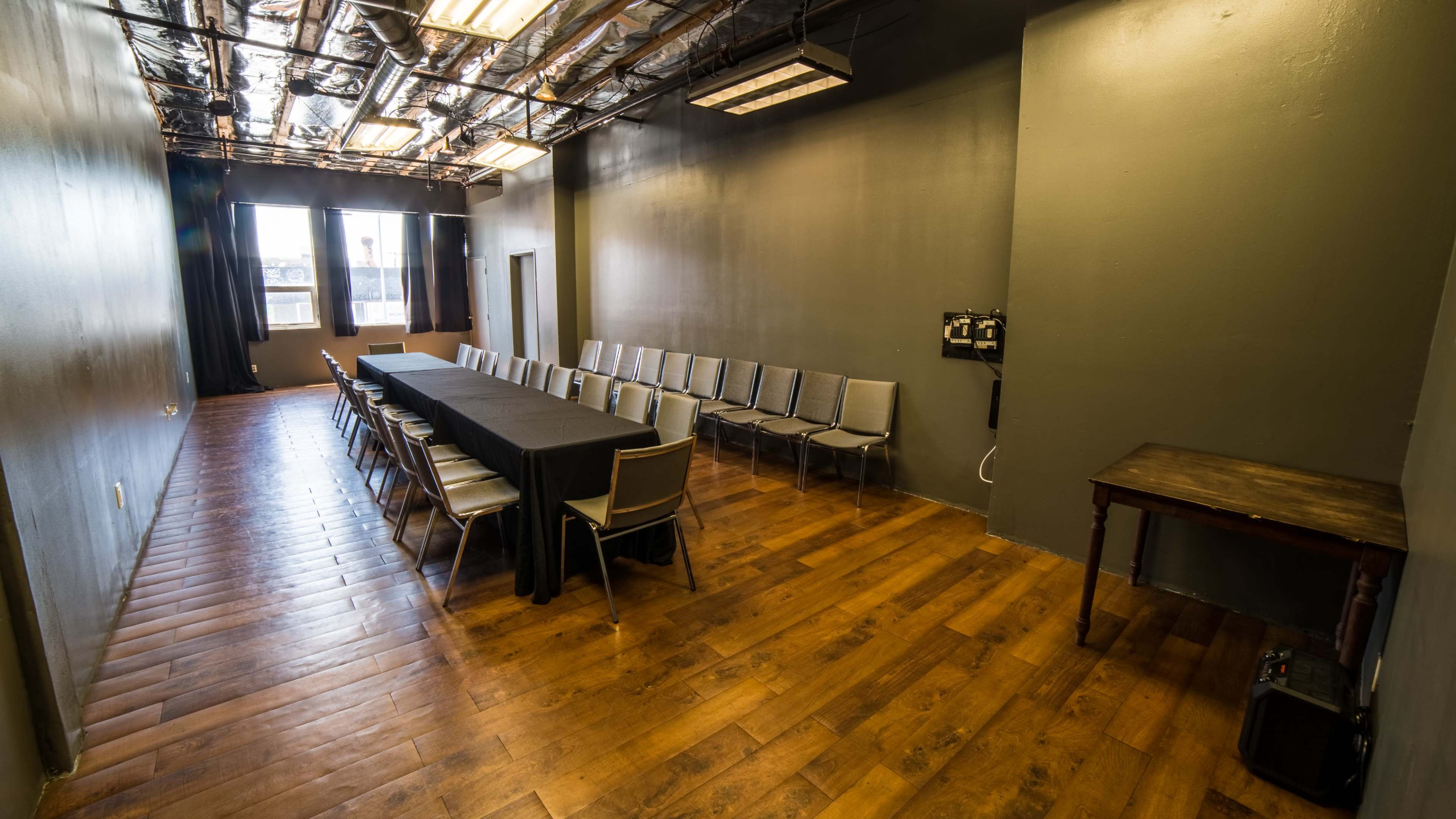 A long, rectangular conference room with a black tablecloth covering a table and rows of chairs along the walls, featuring wooden flooring and large windows providing natural light.