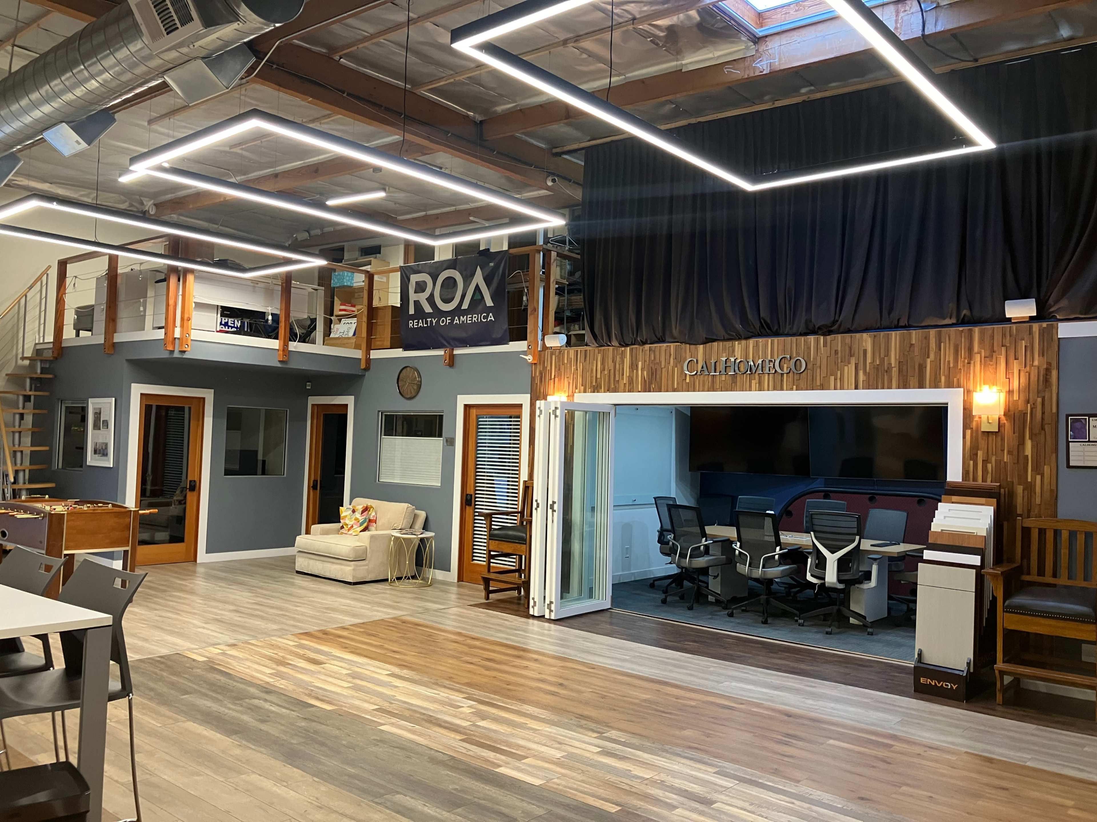 The image depicts an office space featuring modern decor, a lounge area with a couch, meeting rooms, and an open layout illuminated by overhead lights.