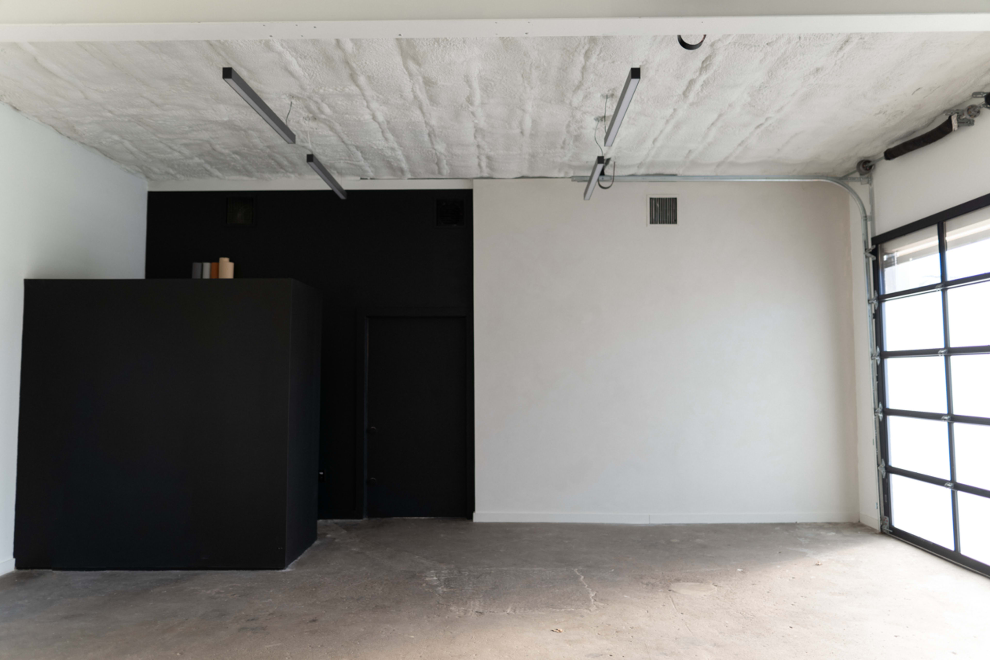 A minimalist interior space with a black wall structure, a white wall, and a large glass garage door.