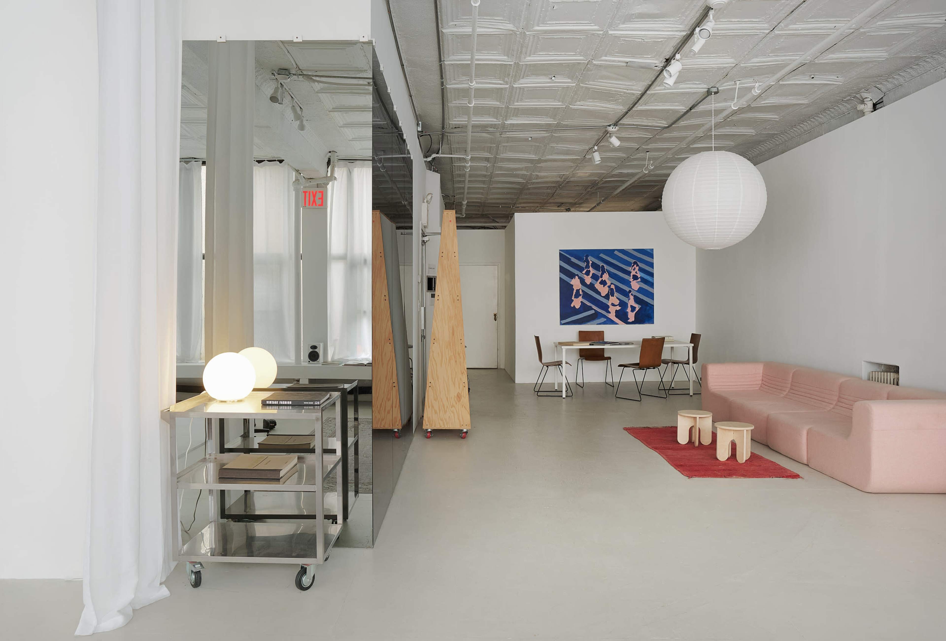 The image depicts a modern, minimalist interior space featuring a seating area with a pink sofa, dining table, and contrasting light fixtures.