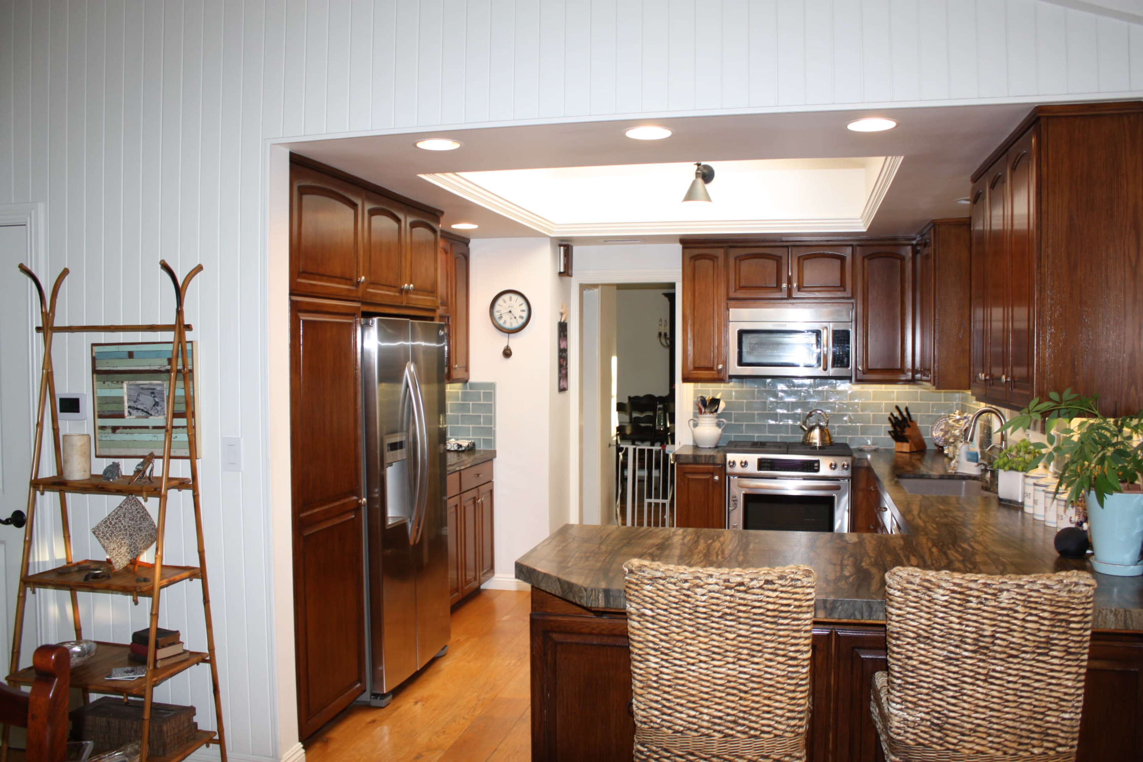 The image shows a modern kitchen with dark wood cabinetry, a large island with woven bar stools, and stainless steel appliances.