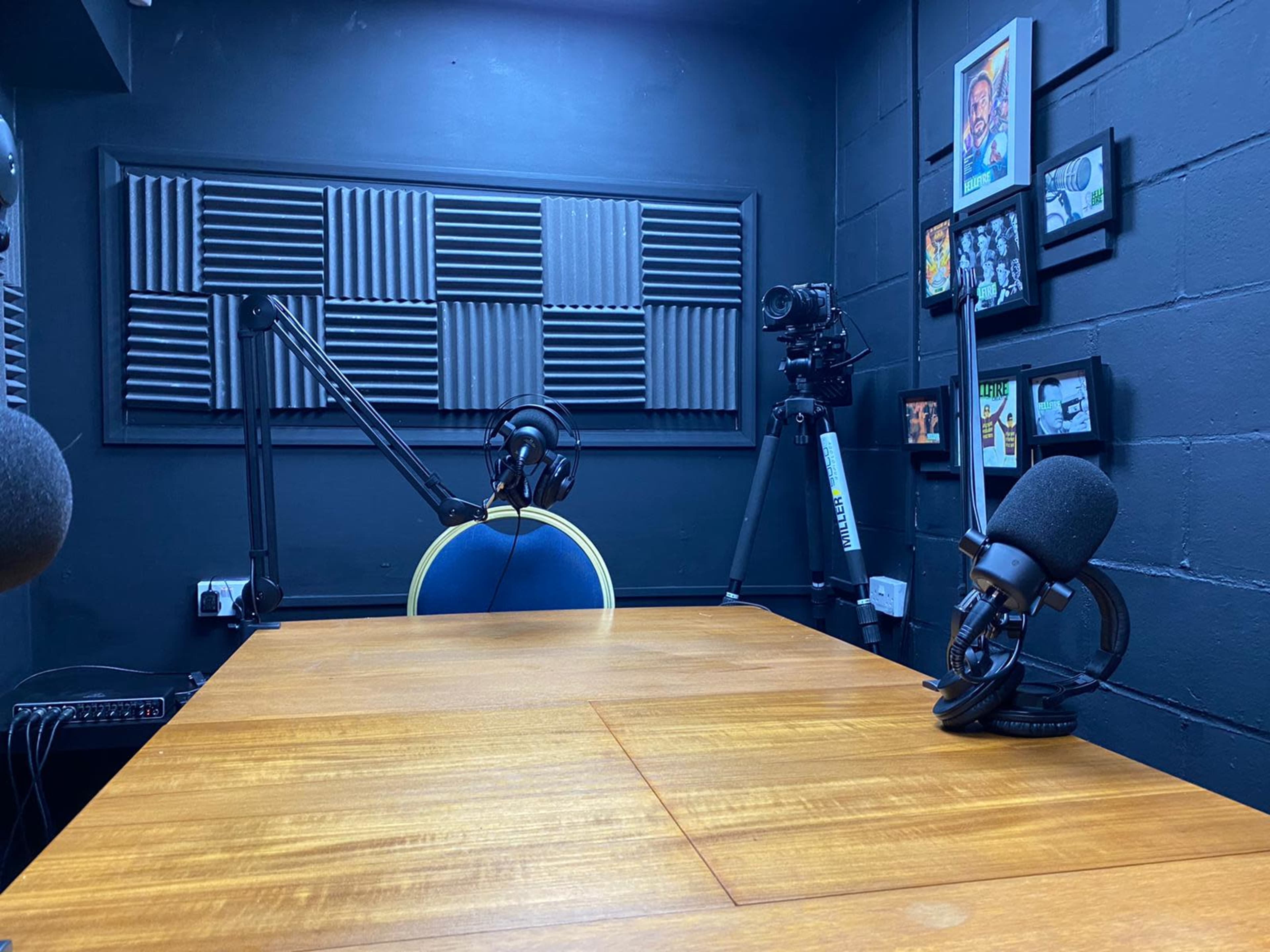 A recording studio with a wooden table, microphone setups, a chair, and wall-mounted soundproof panels.