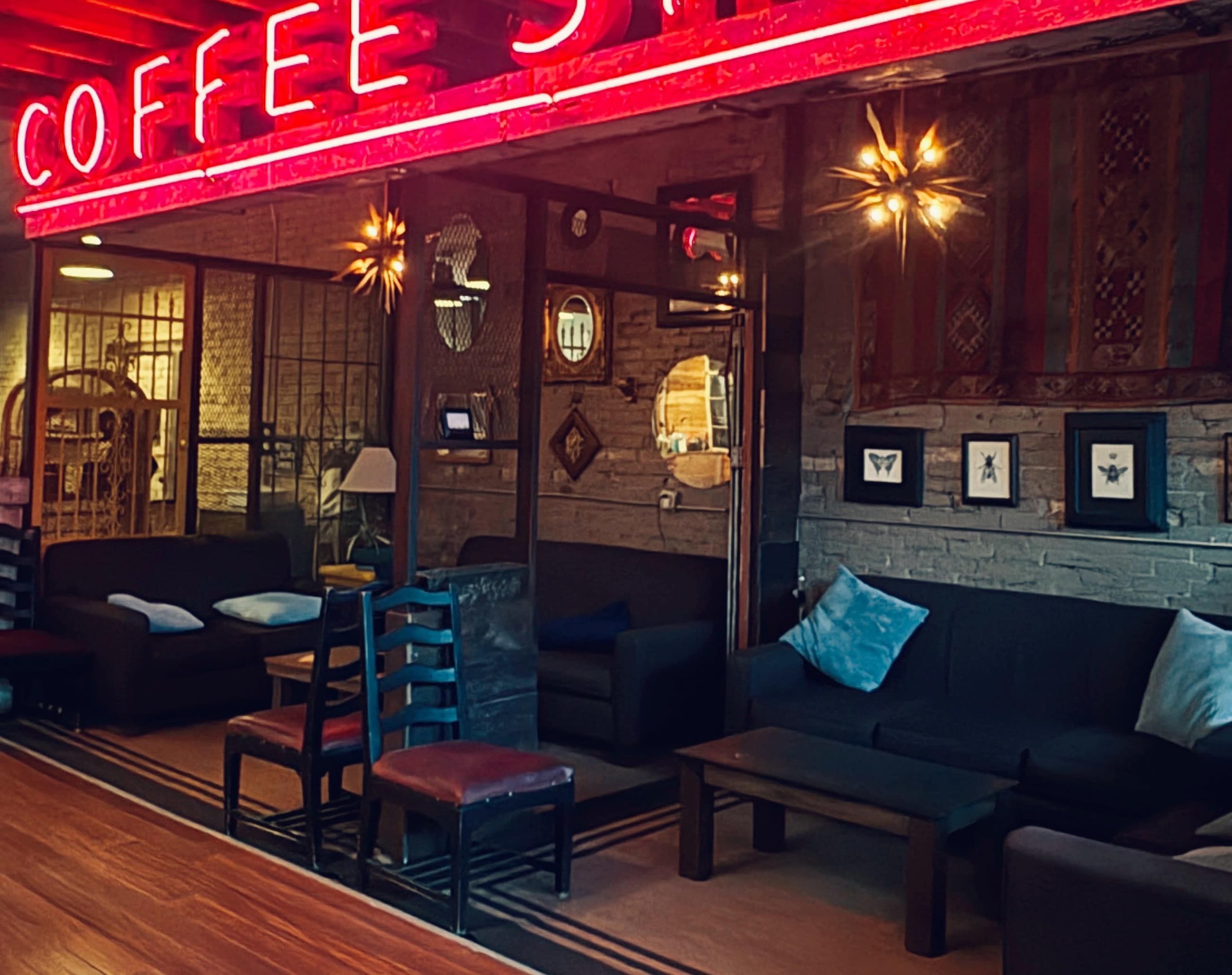 The image shows a coffee shop interior with a neon sign reading "COFFEE ST," featuring dark seating, wooden tables, and decorative wall elements.