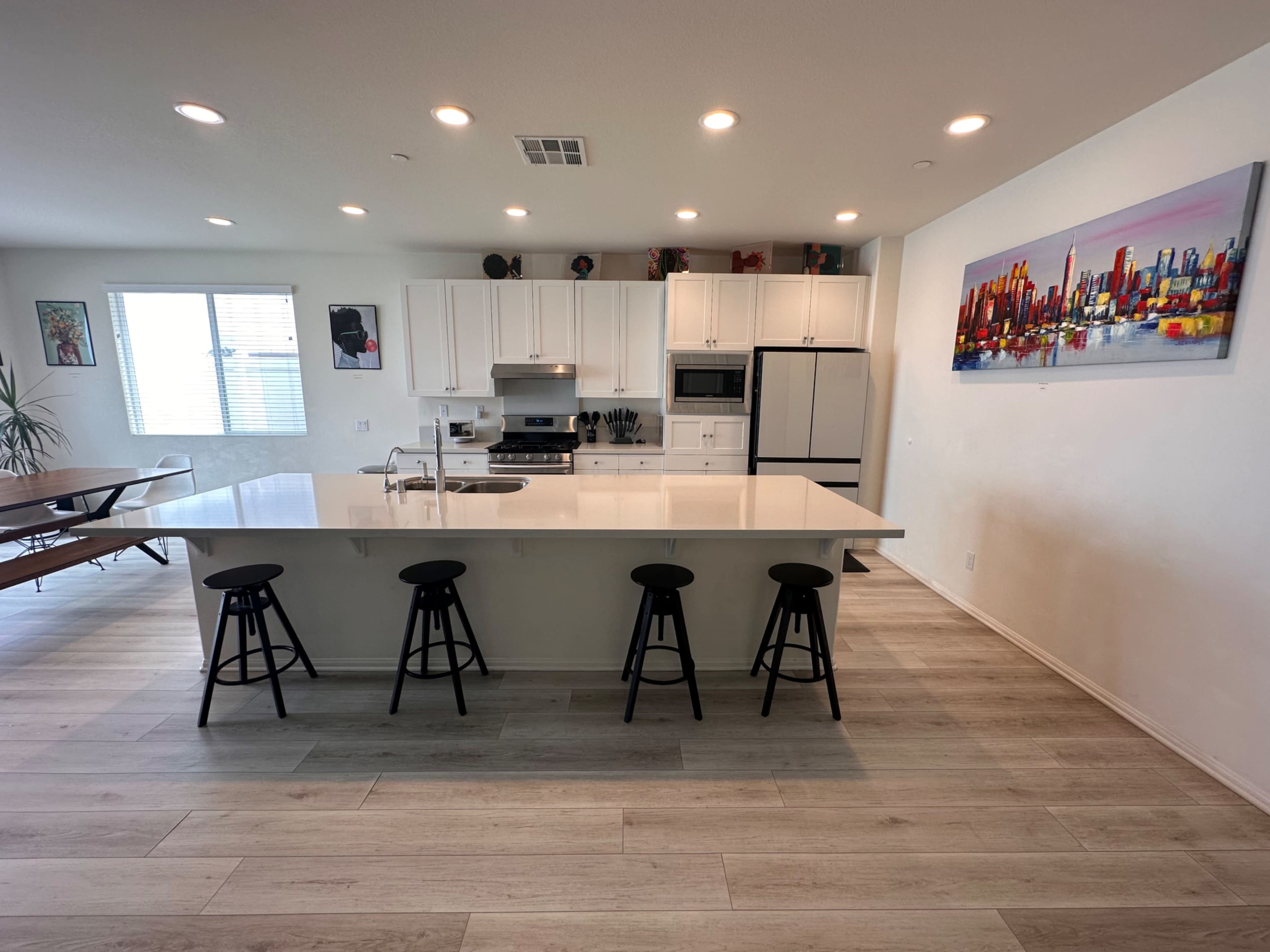 A modern kitchen with white cabinets, a central island with four black stools, and stainless steel appliances.