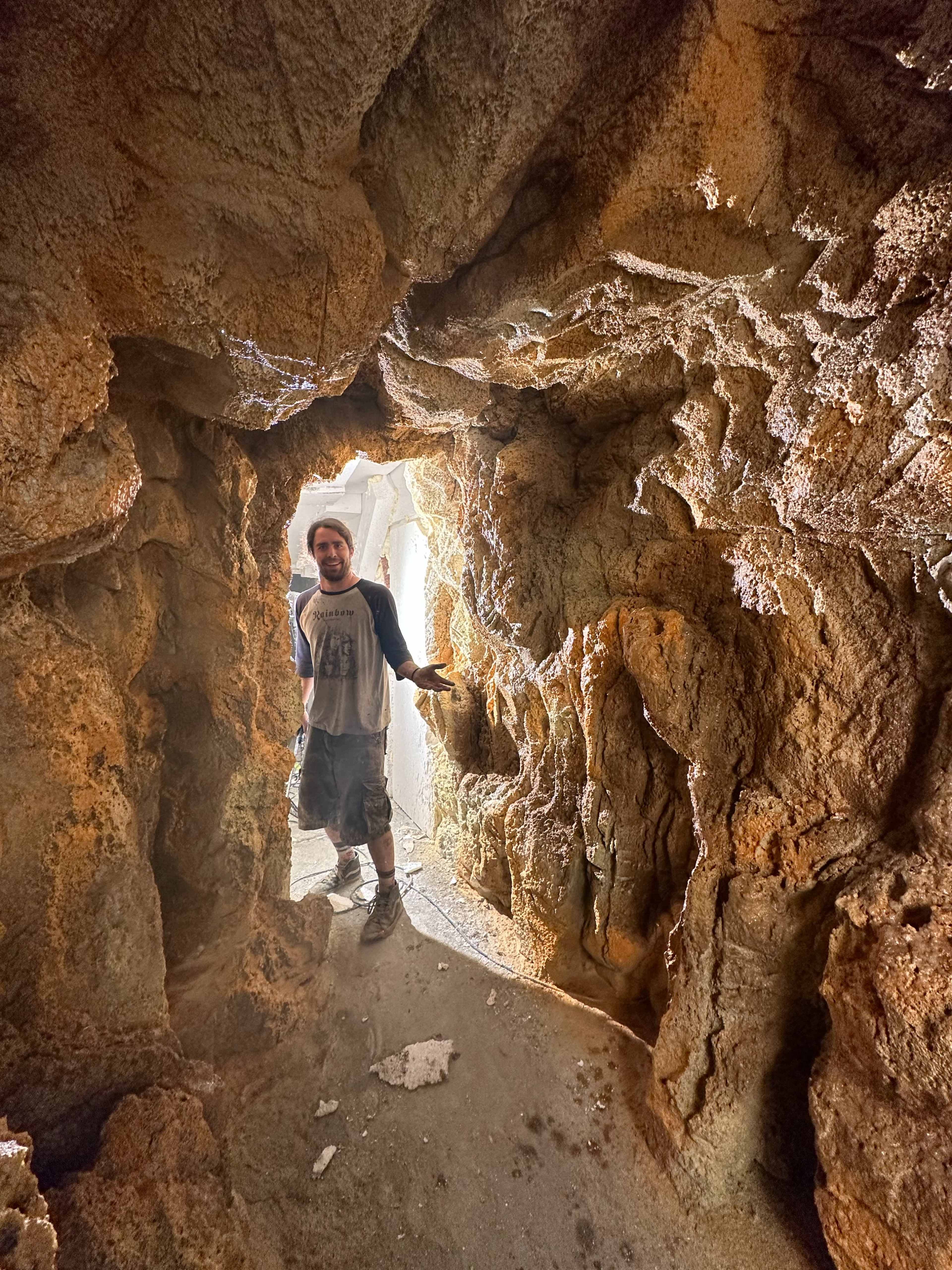 A person stands in a narrow rock passageway with textured walls.