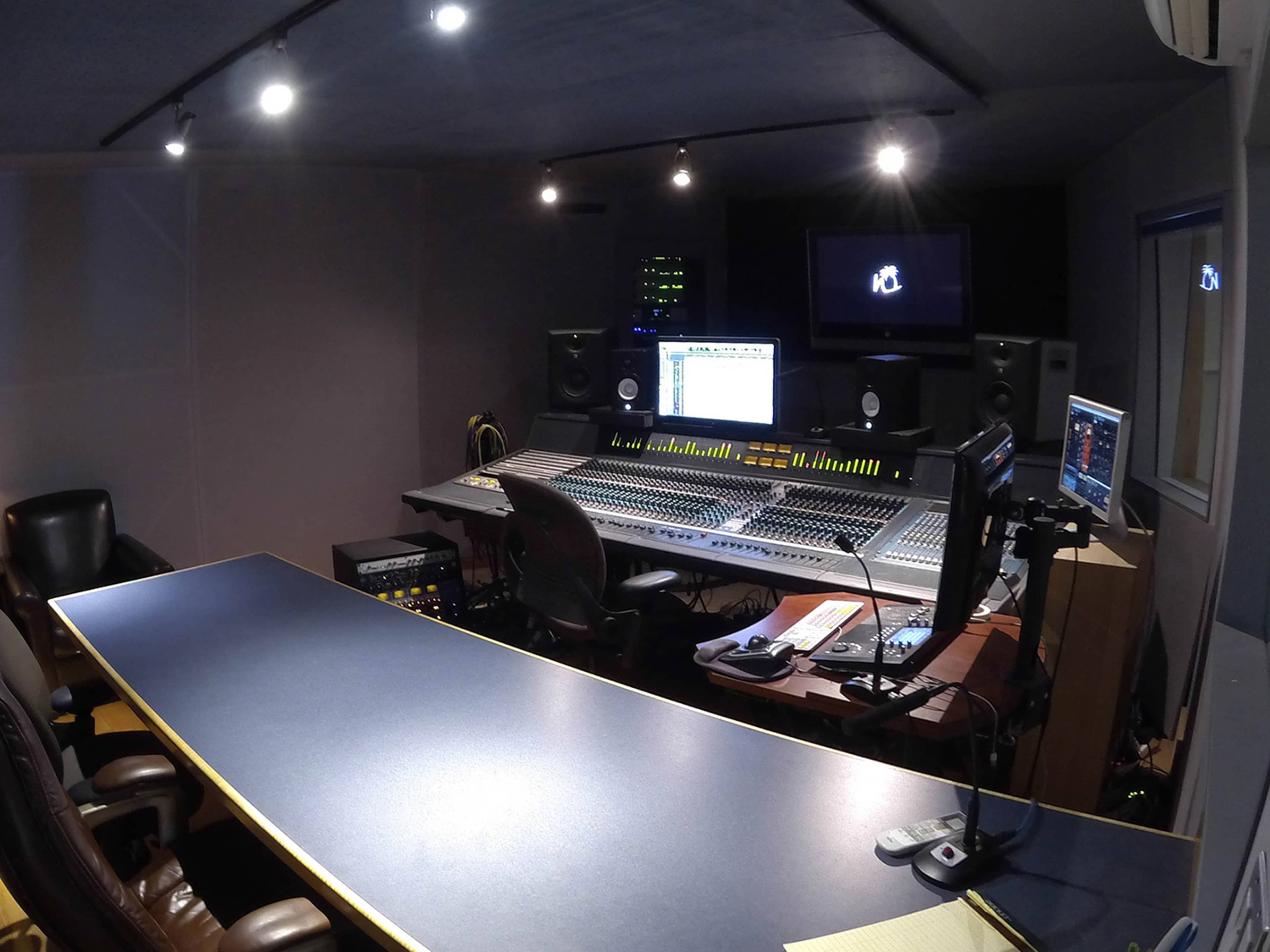 A modern music recording studio with a large mixing console, computer monitors, and audio equipment arranged around a central workspace.