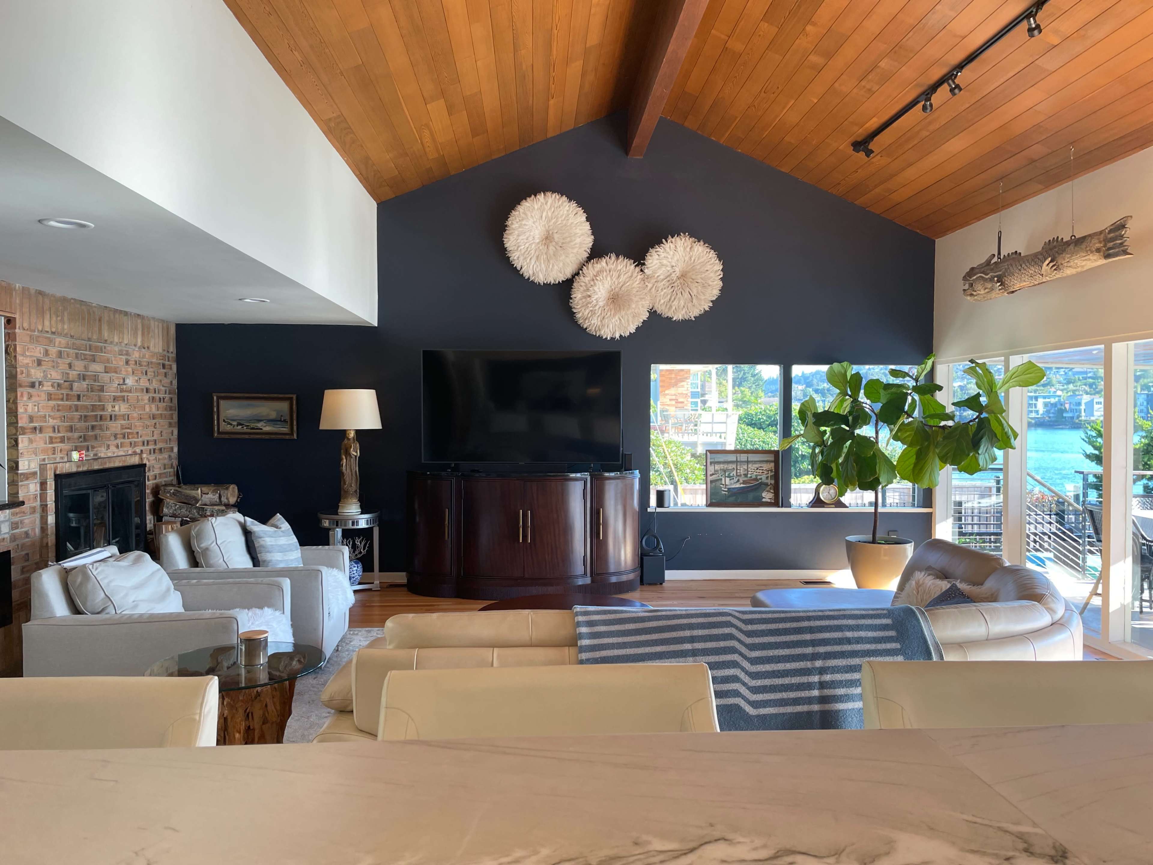 A spacious living room features a dark accent wall, a television on a wooden cabinet, and large windows overlooking a water view.