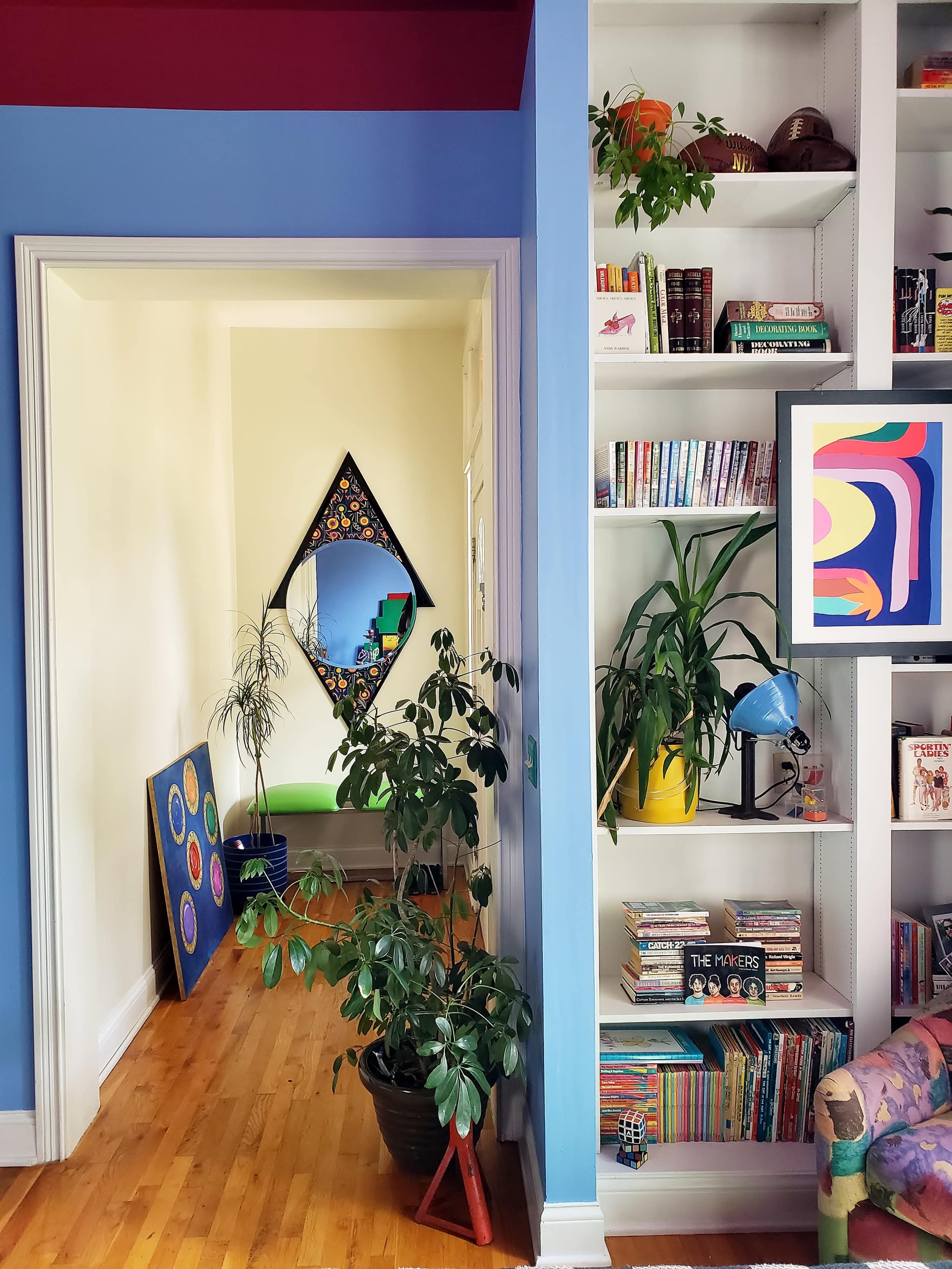 A brightly colored room features a hallway leading to a small space with artwork on the walls and bookshelves filled with books and decorative items.