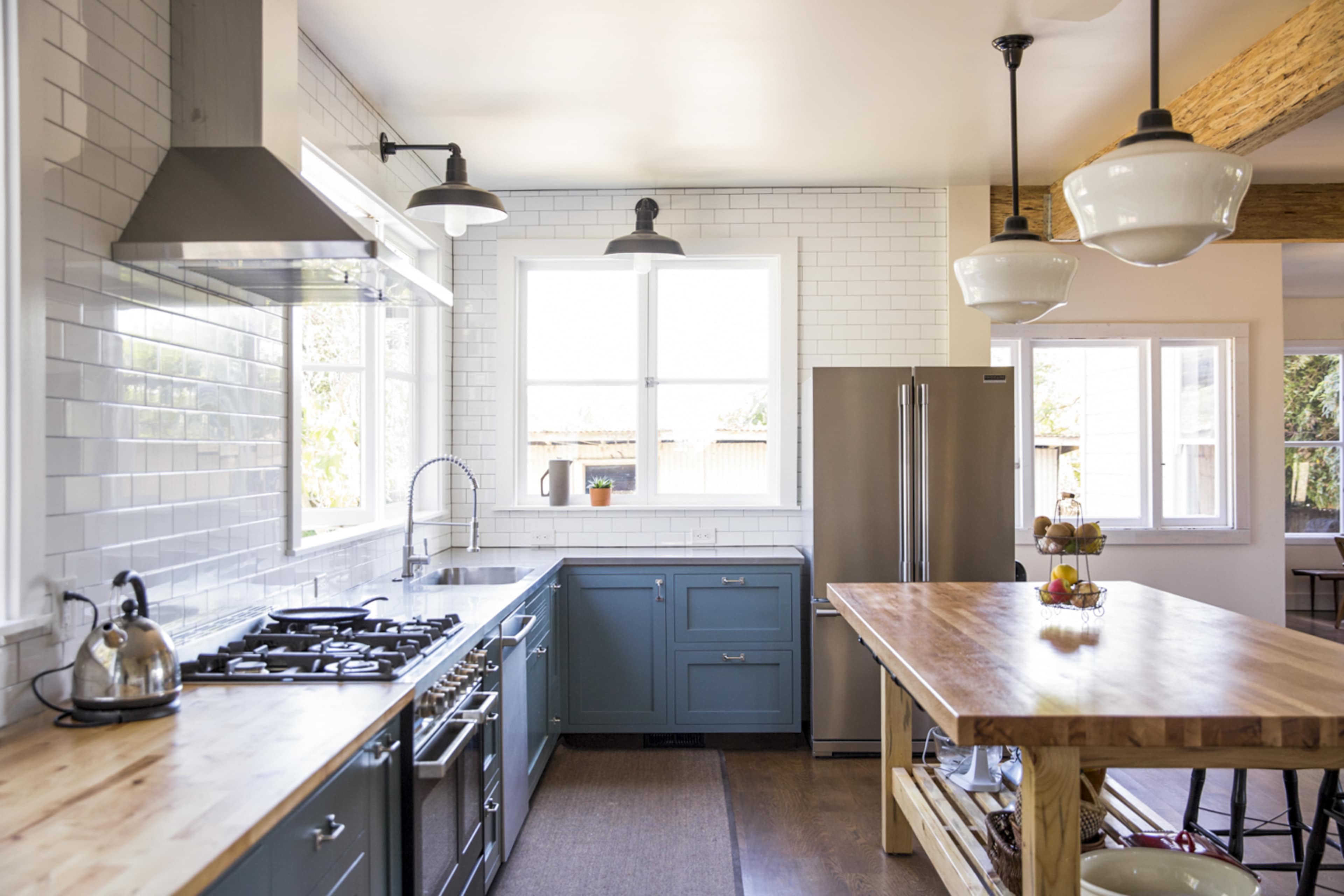 The kitchen features blue cabinets, stainless steel appliances, a wooden island, and large windows that provide natural light.