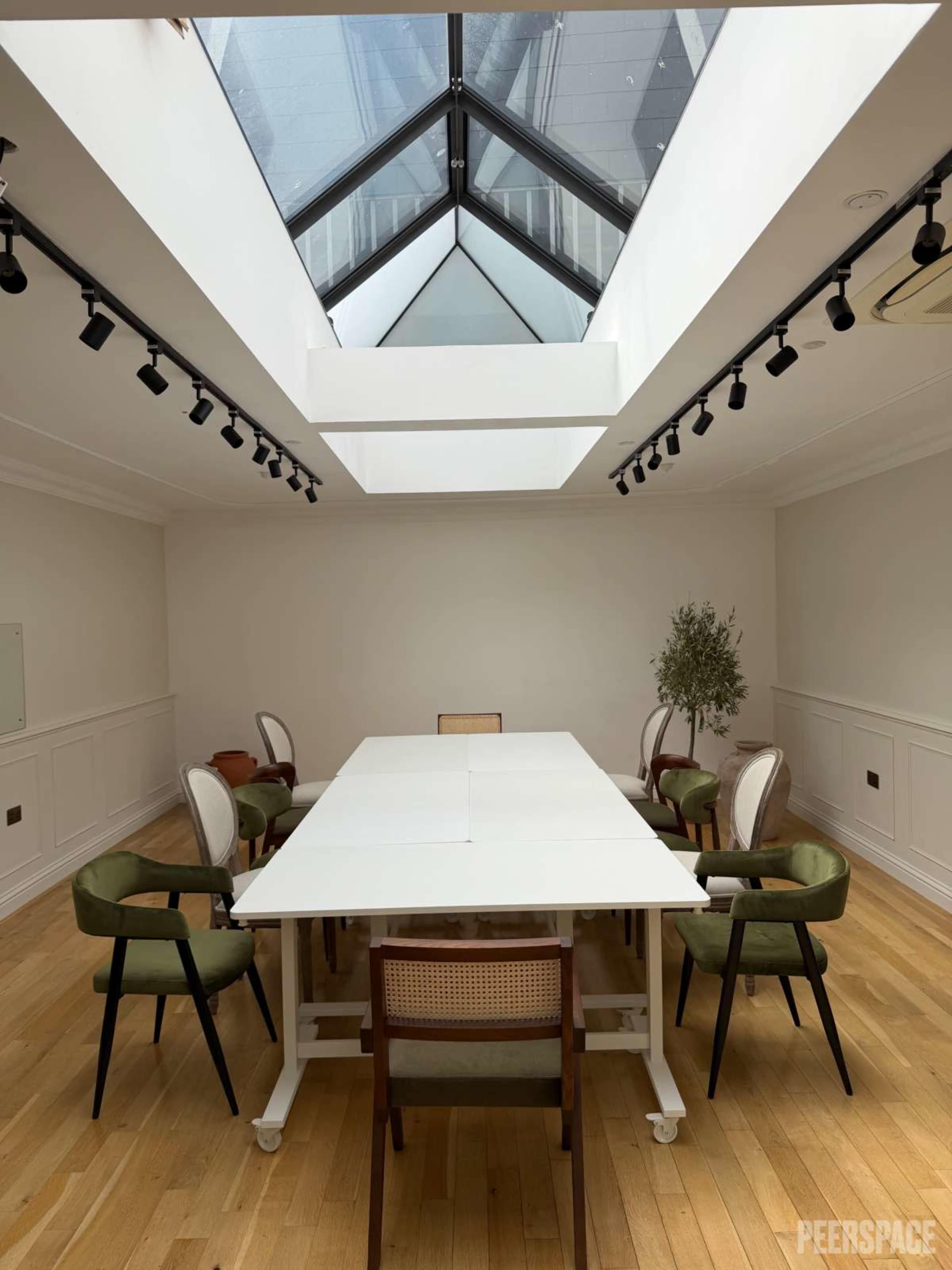 A large, minimalist conference room features a long white table surrounded by chairs and a skylight above.