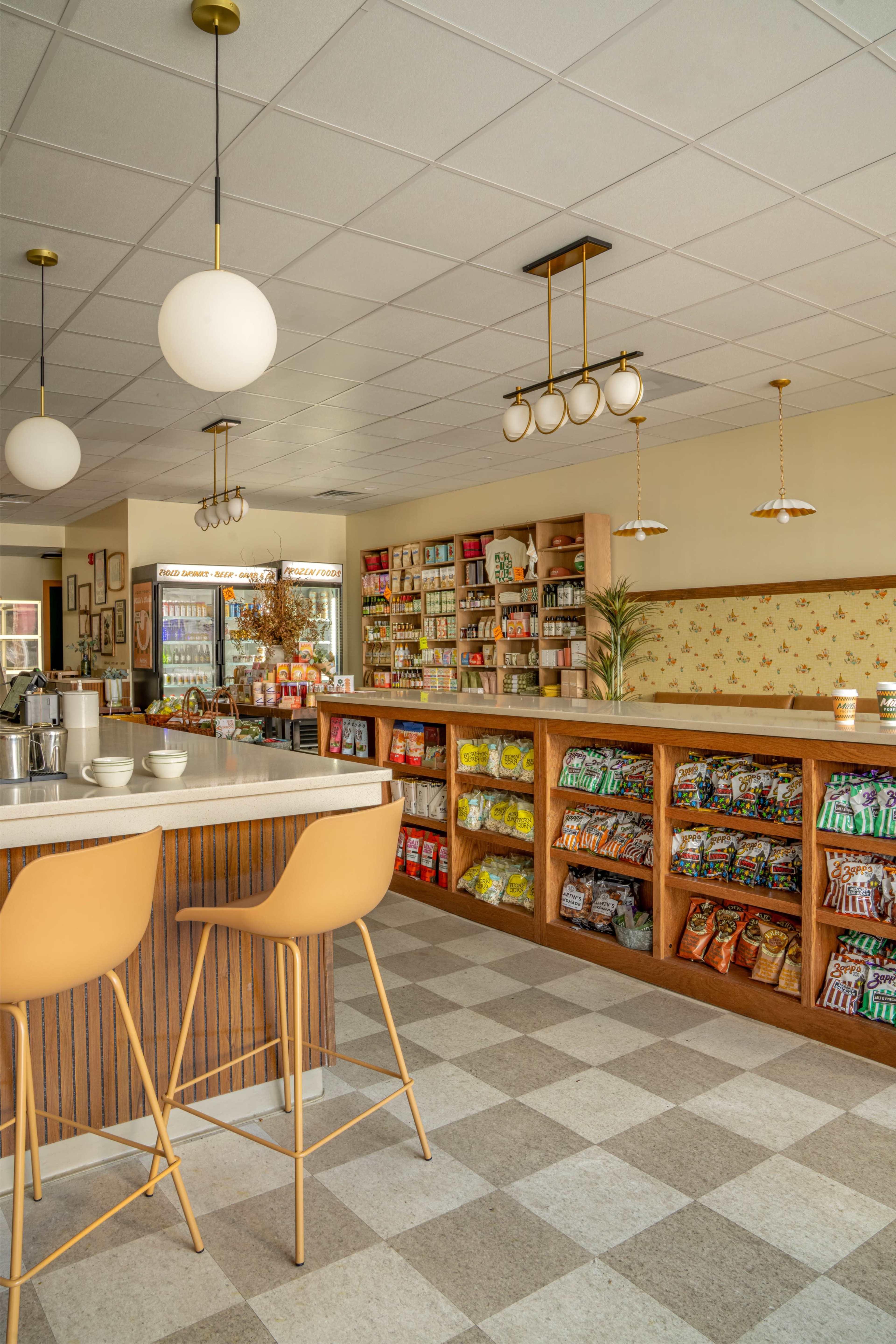The image shows a brightly lit café with a service counter and shelves stocked with various packaged goods.
