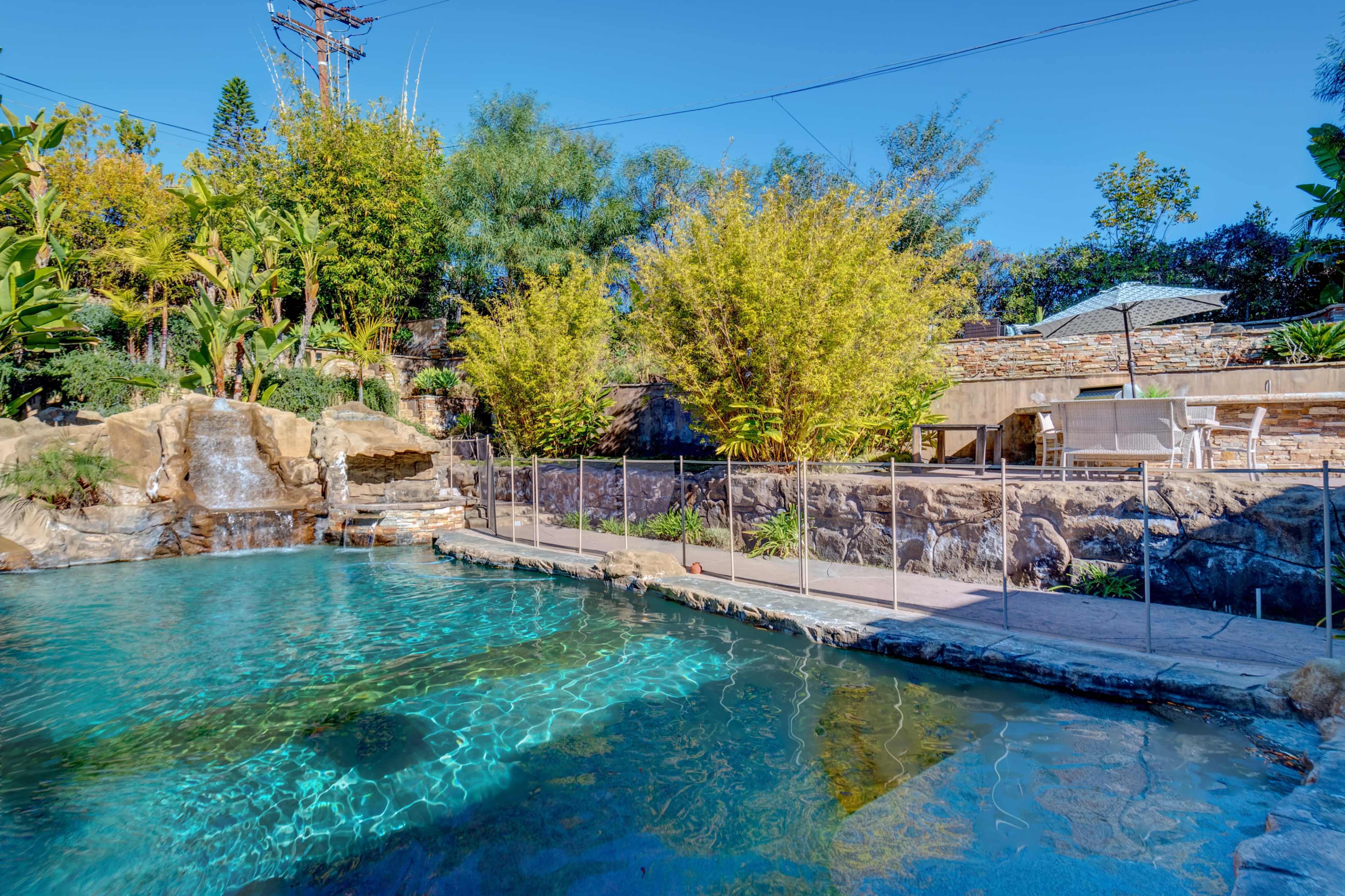 A landscaped swimming pool area with a rock waterfall and surrounding lush greenery.