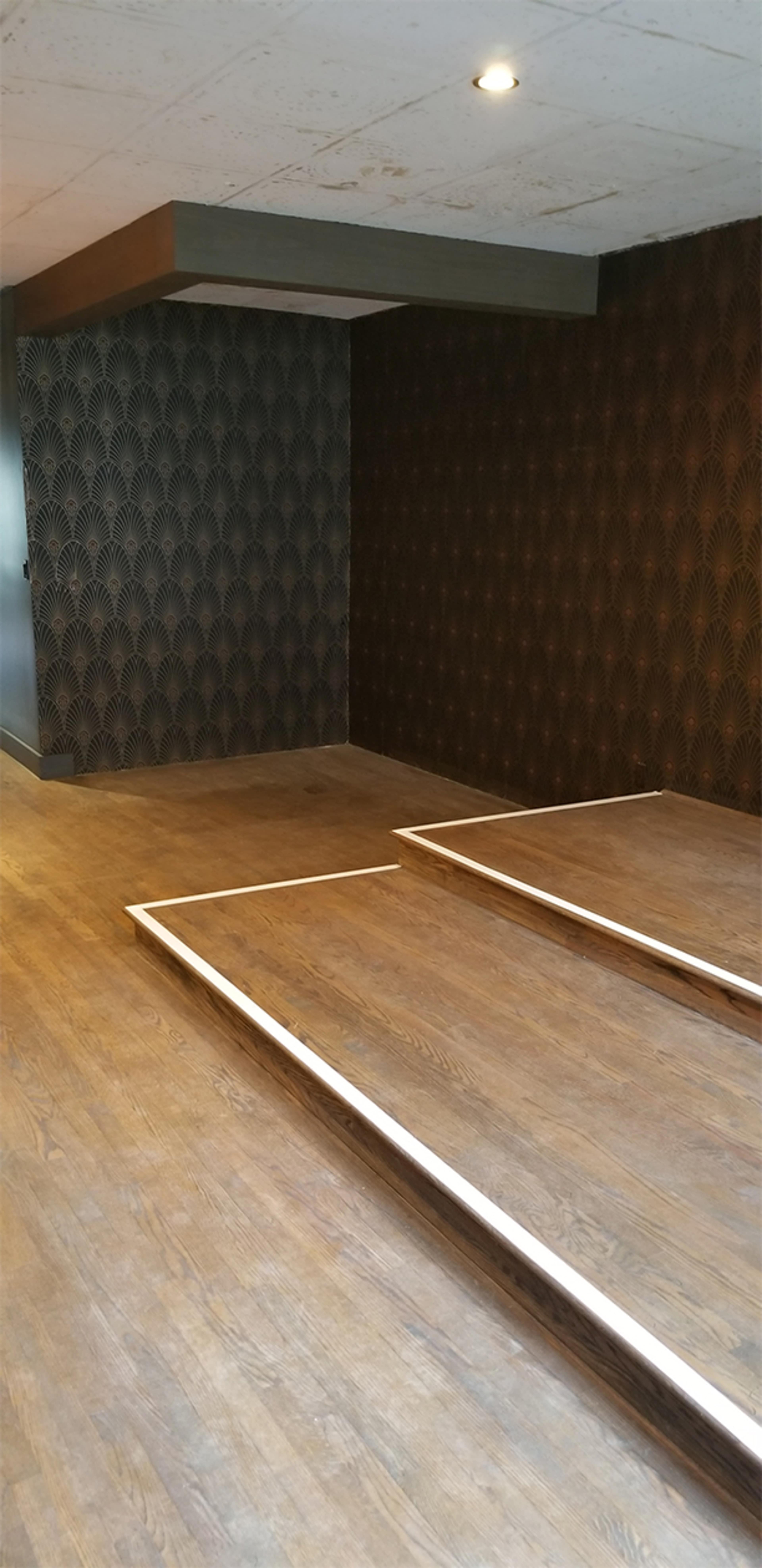 The image shows an unfinished room with two wooden frames on the floor, surrounded by patterned walls and a ceiling light.