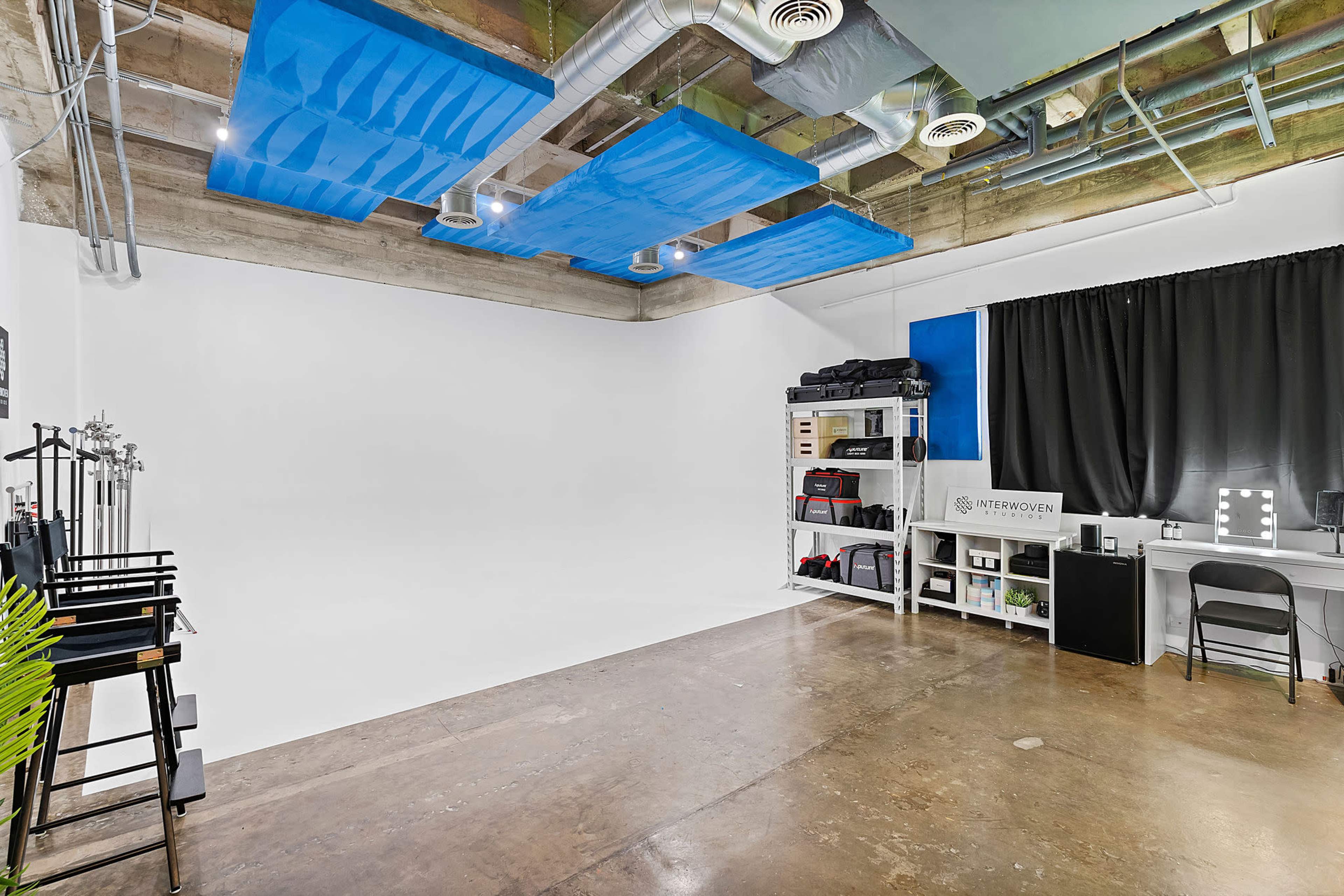 A minimalistic studio space featuring a white backdrop, concrete flooring, and various equipment arranged along the wall.